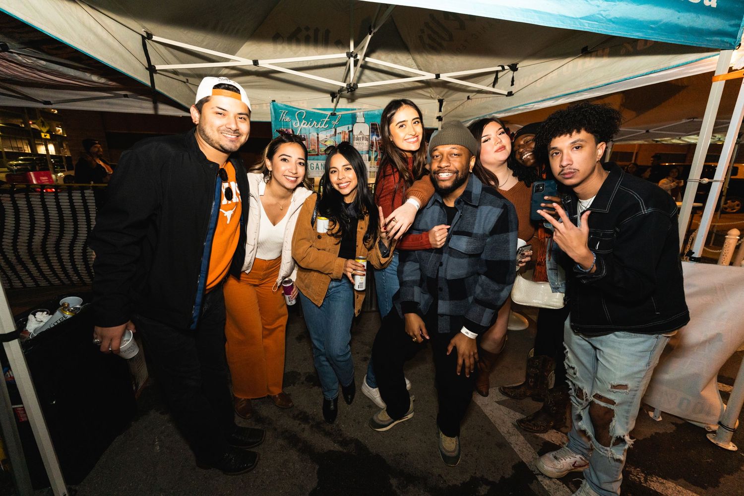 Friends gathered under a blue tent at night showing peace signs and smiling.
