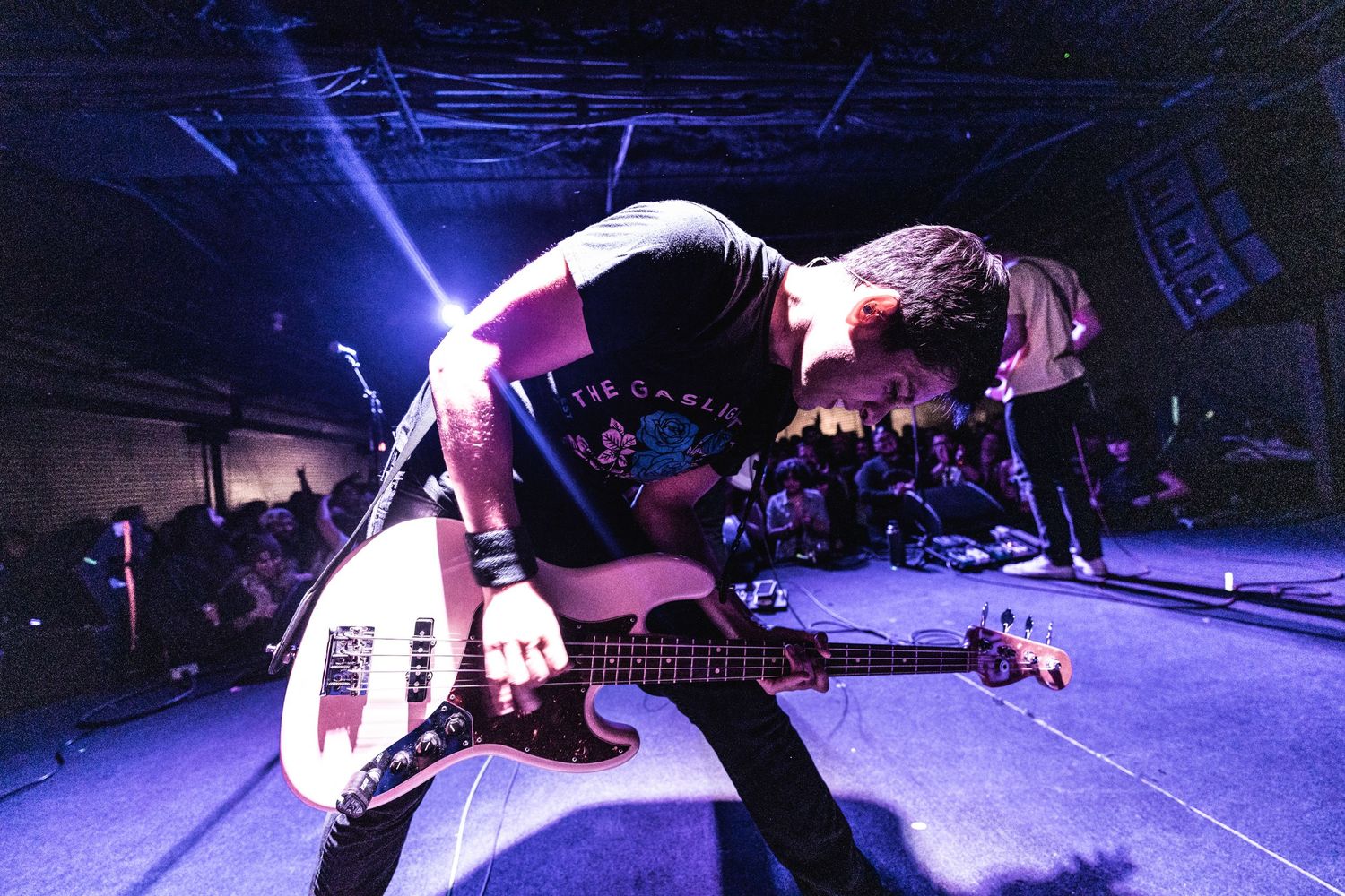 Musician bends backward while playing bass guitar under purple stage lighting.