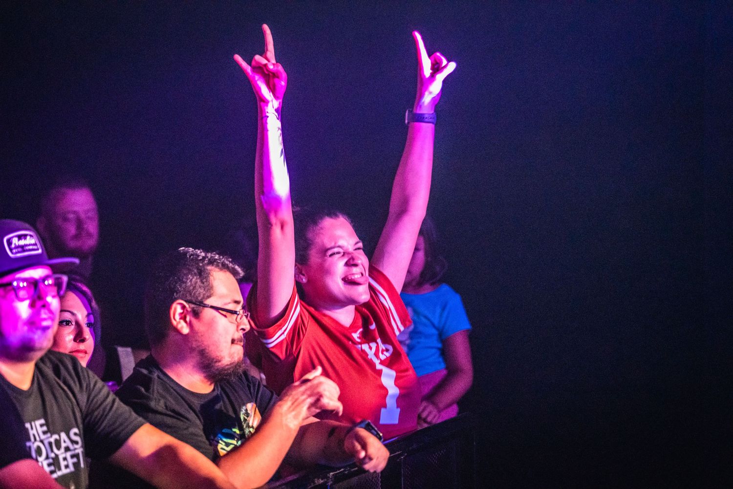 Concert crowd cheers enthusiastically with hands raised during an energetic performance.