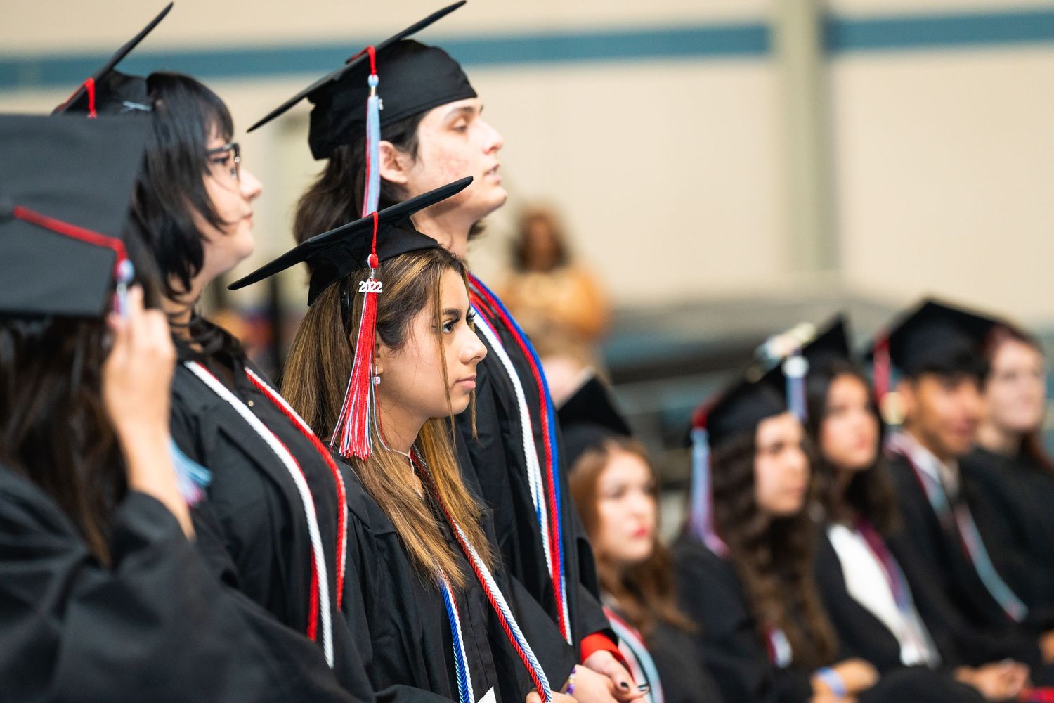 Row of graduates in black caps and gowns at graduation ceremony.
