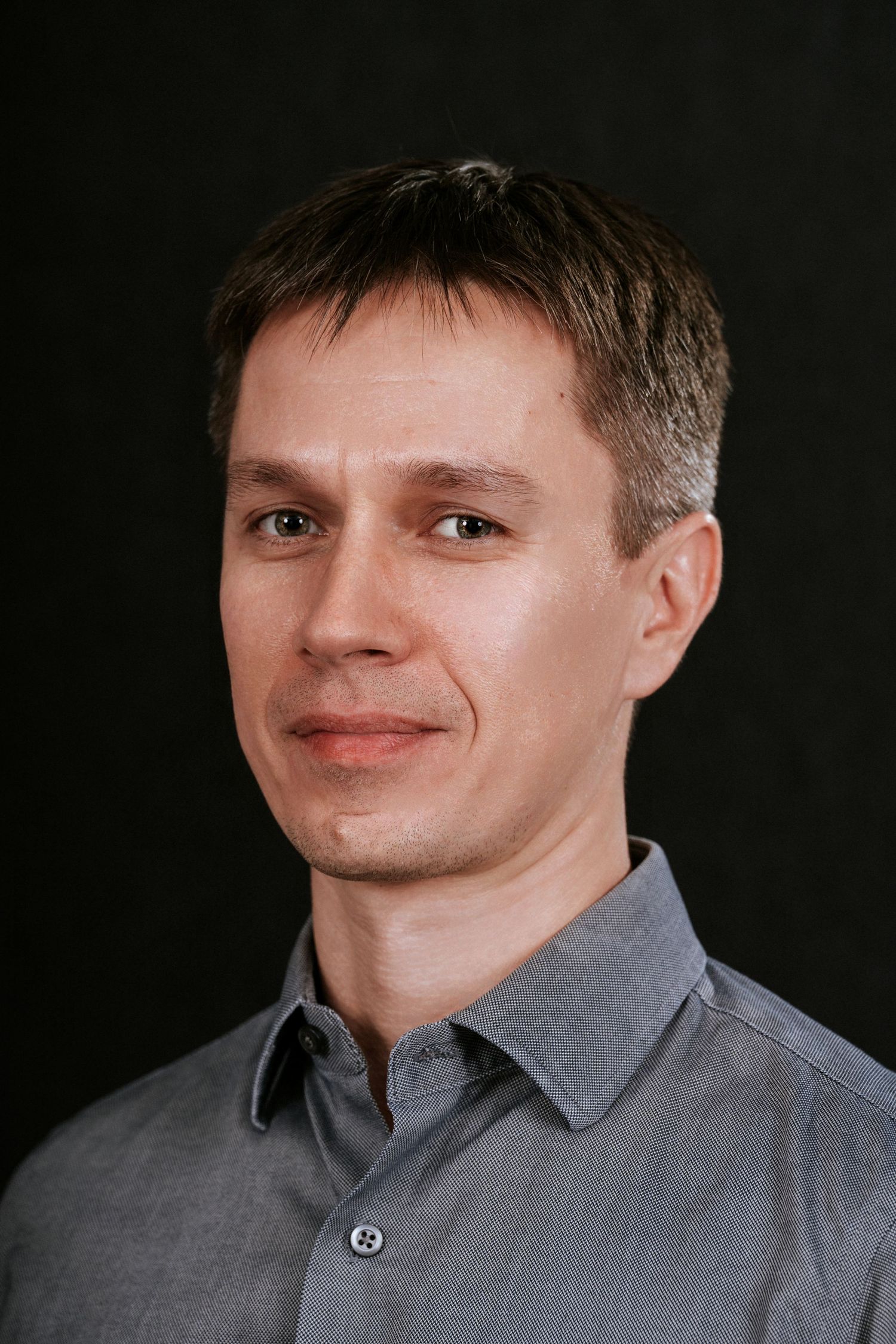 Studio portrait of person in grey collared shirt against black background.