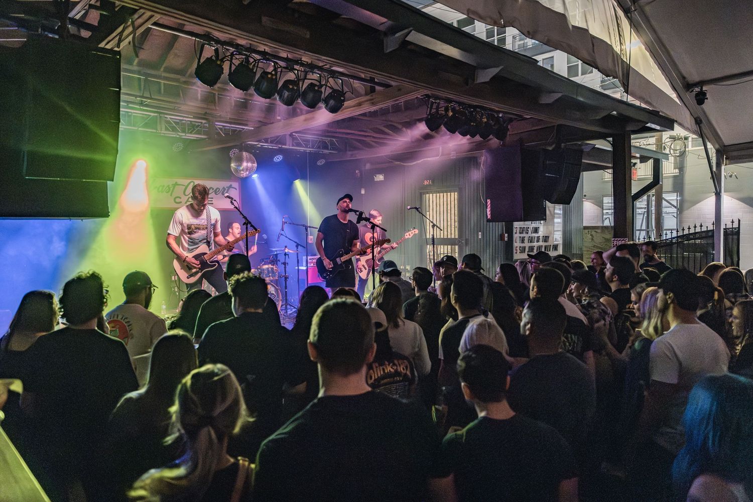 Wide shot of a rock concert with band performing on stage and crowd silhouettes in foreground.