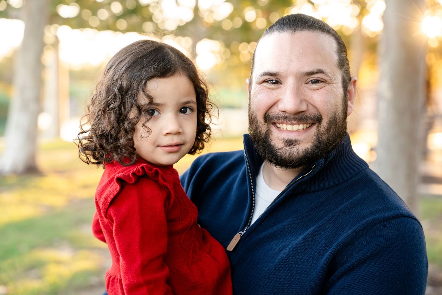 Parent and child in coordinating navy and red outfits smiling outdoors.