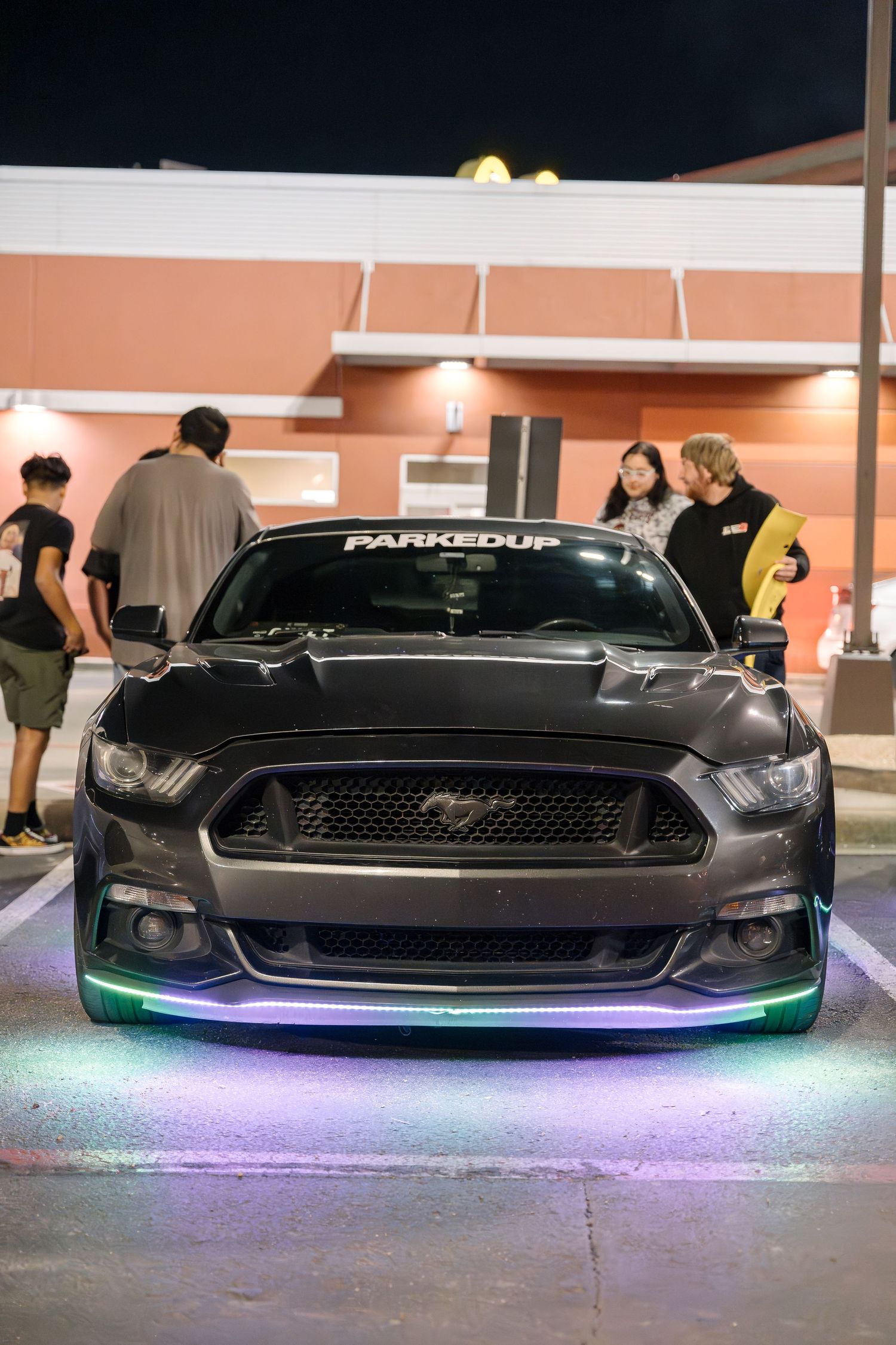 A modified Ford Mustang with purple underglow lighting and custom decals parked at night.