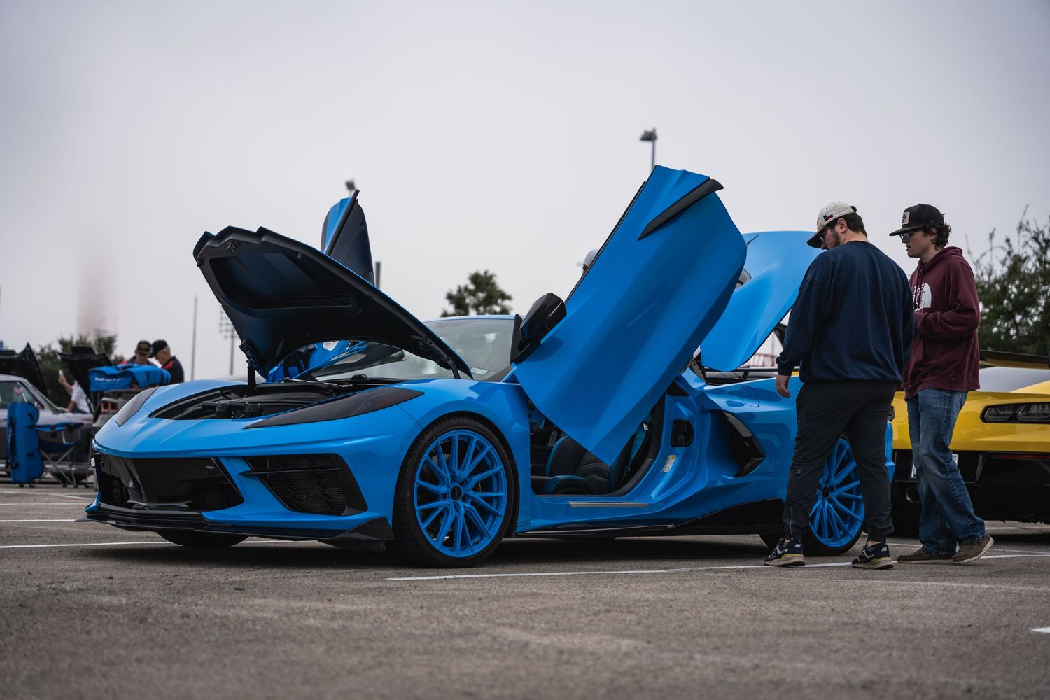 Blue Chevrolet Corvette C8 with scissor doors open on display at car meet.