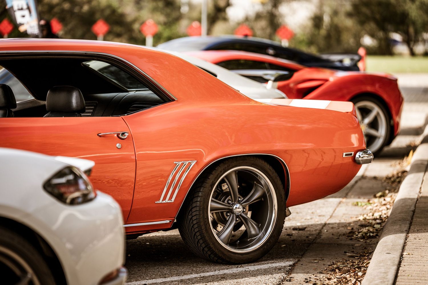 Close up view of a classic orange muscle car's side profile with custom wheels parked at a car show.