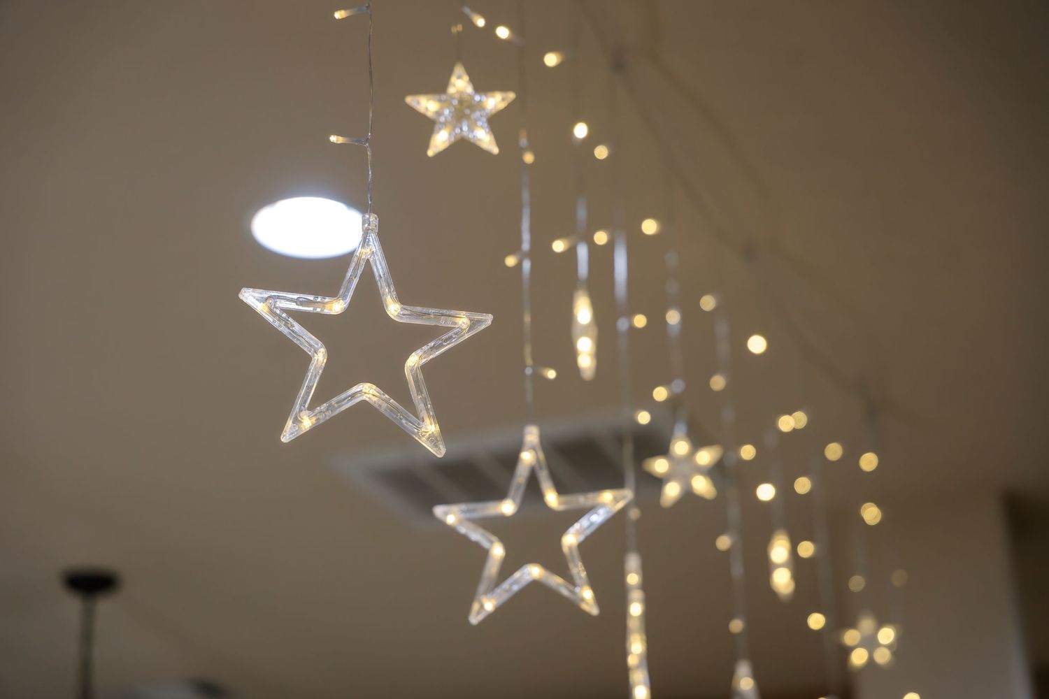 Illuminated star decorations hanging from ceiling with twinkling lights in background.