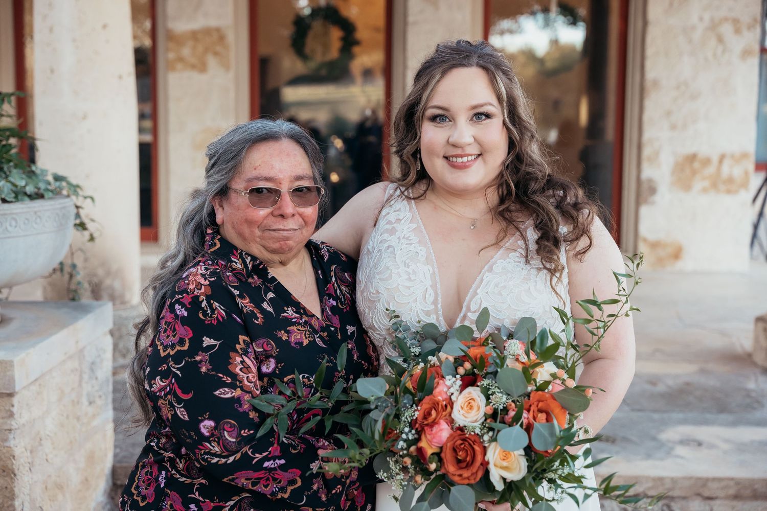Wedding portrait with beautiful peach and greenery bouquet against stone architecture.