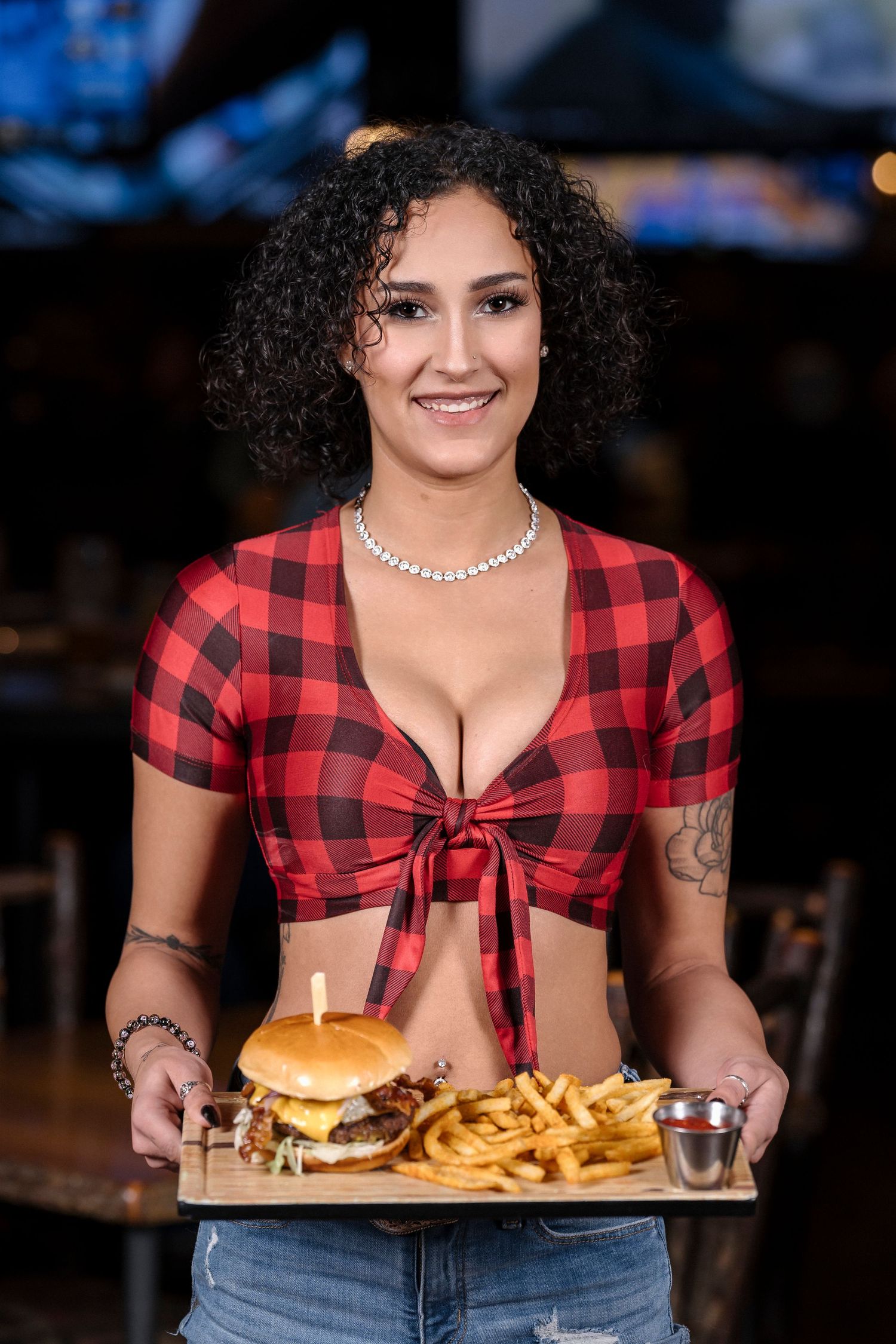 Restaurant server holding burger and fries platter in red checkered crop top.