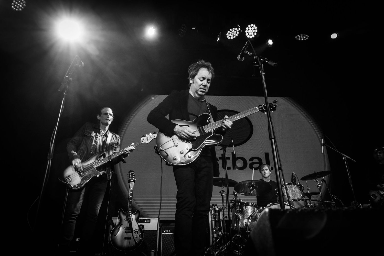 Black and white concert photo showing band performing on stage with dramatic lighting.
