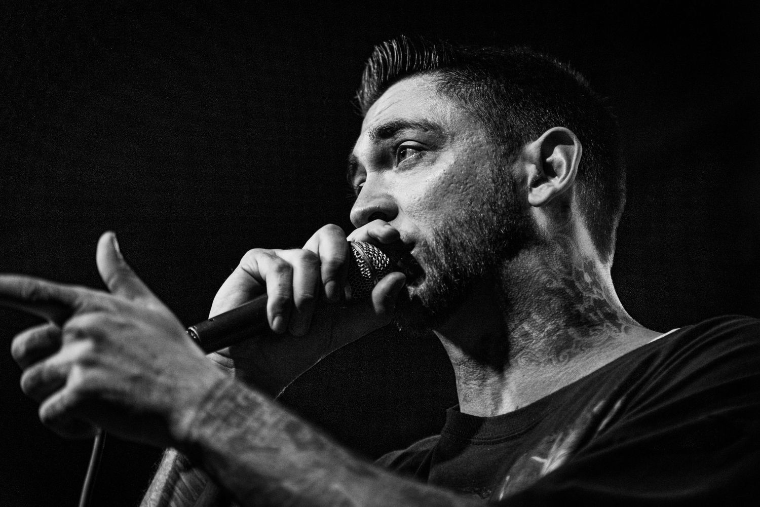 Black and white profile shot of performer speaking into microphone on stage.