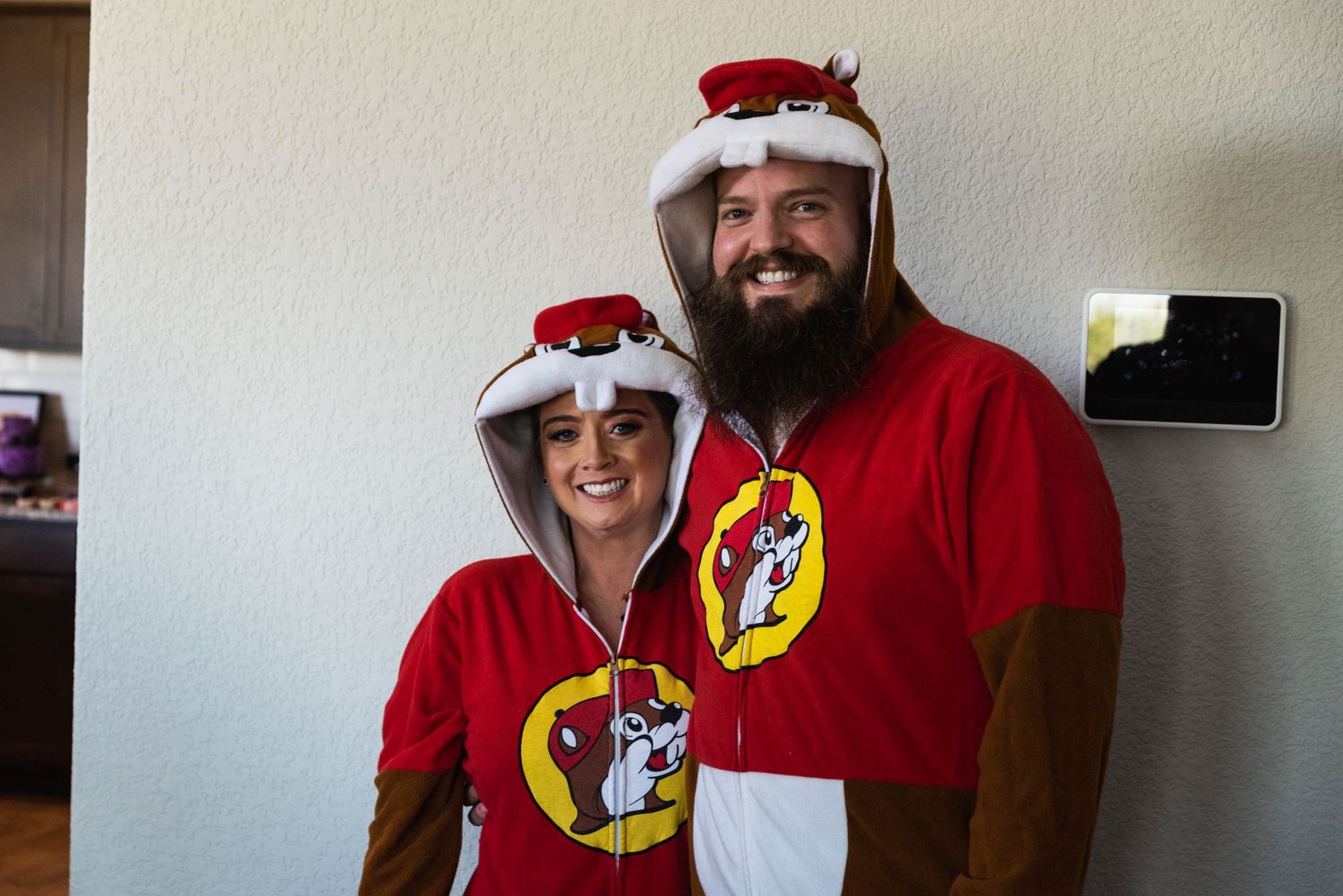 Two people wearing matching red Flash themed Christmas onesies with Santa hats pose together.