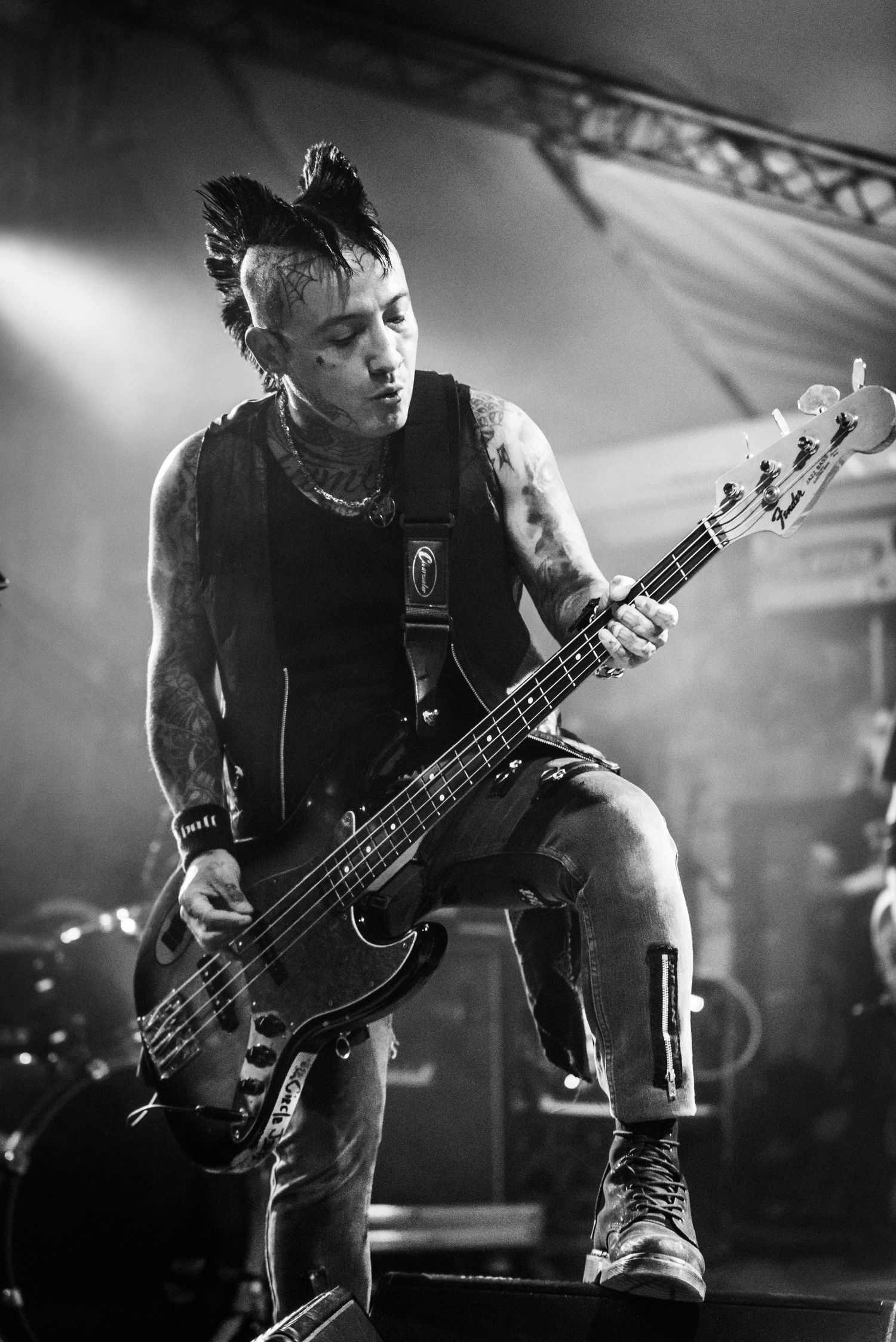 Punk bassist with mohawk performs on dark stage in dramatic black and white concert photo.