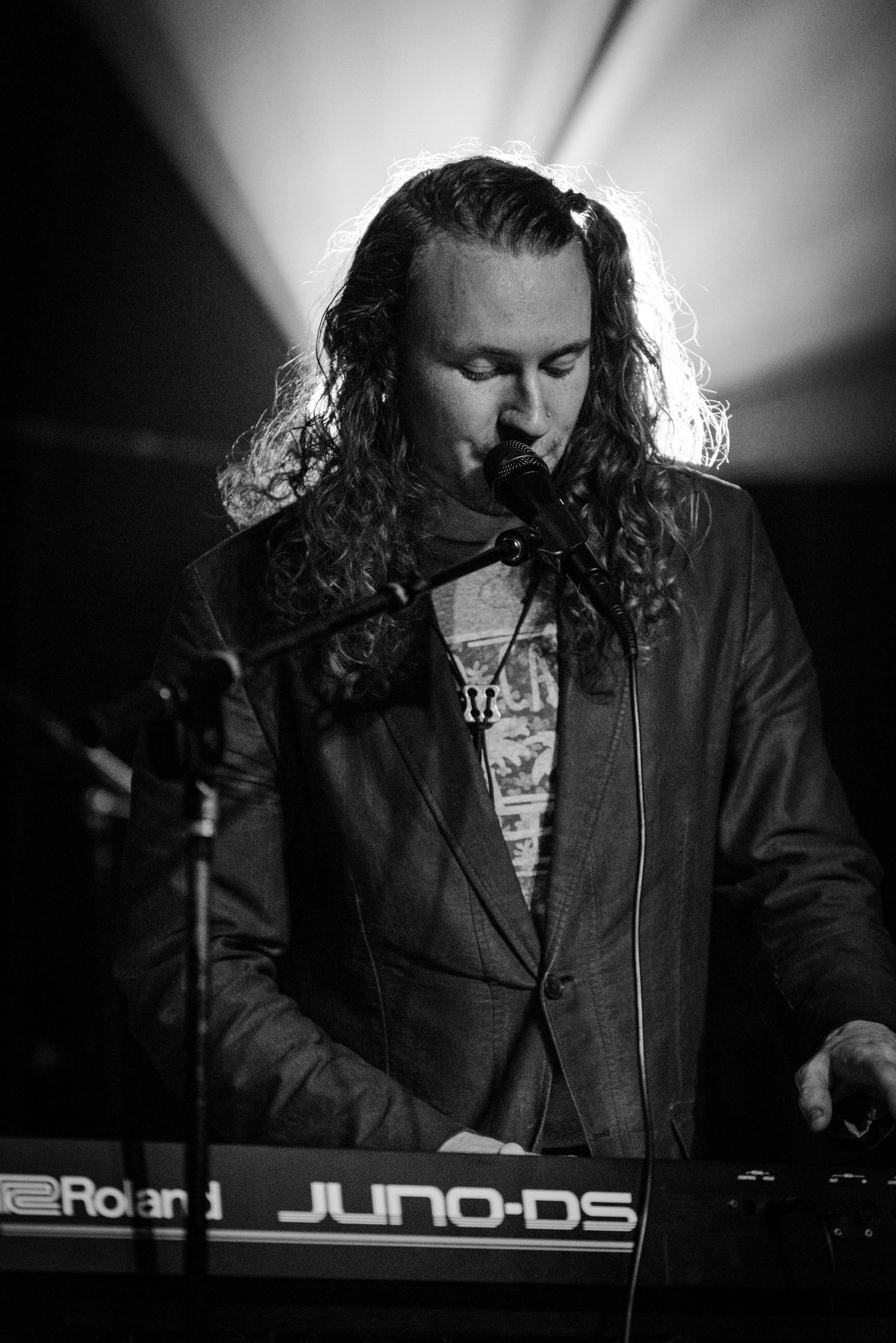 A musician plays keyboard under dramatic black and white stage lighting.