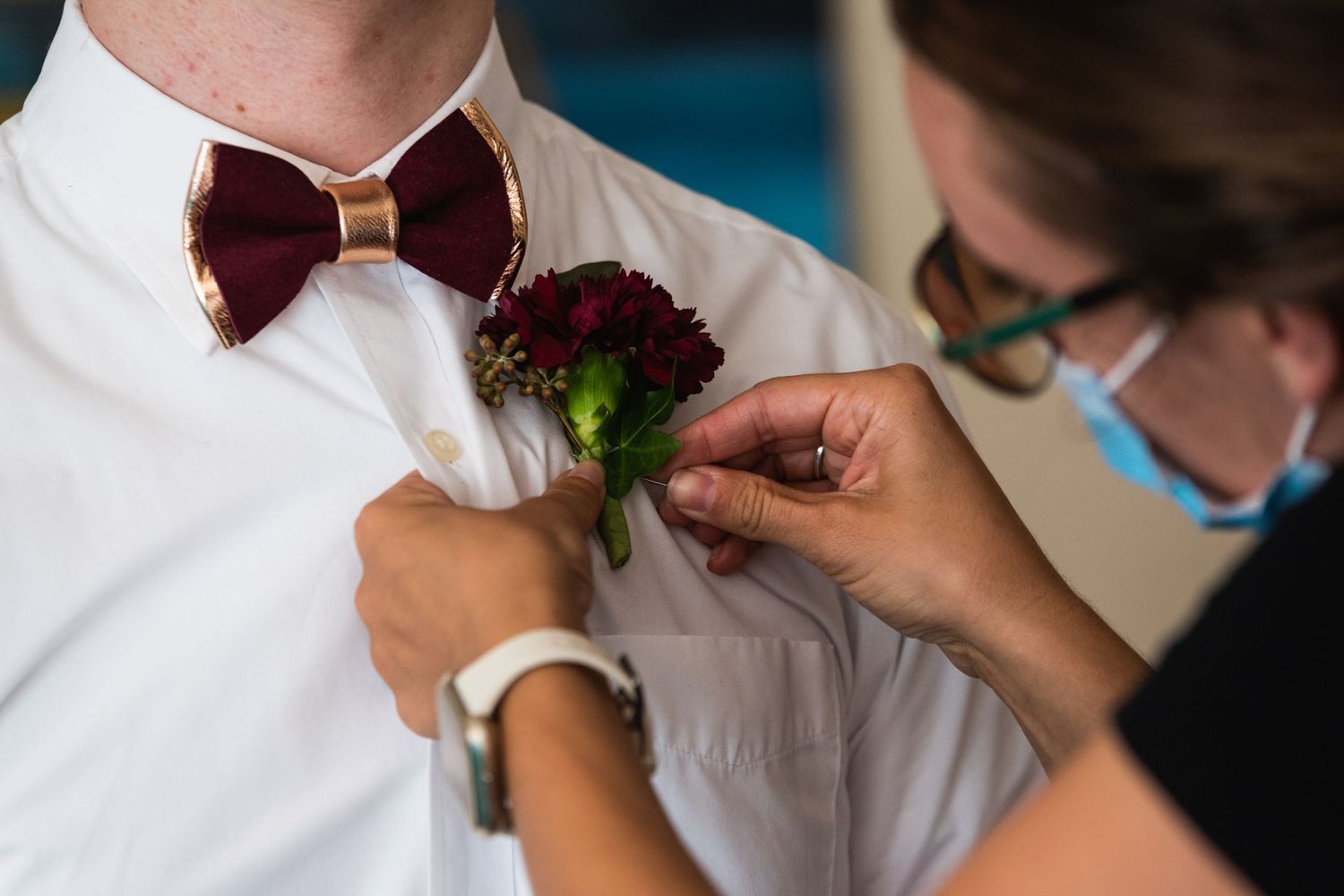 Close-up of hands pinning burgundy boutonniere to white dress shirt.
