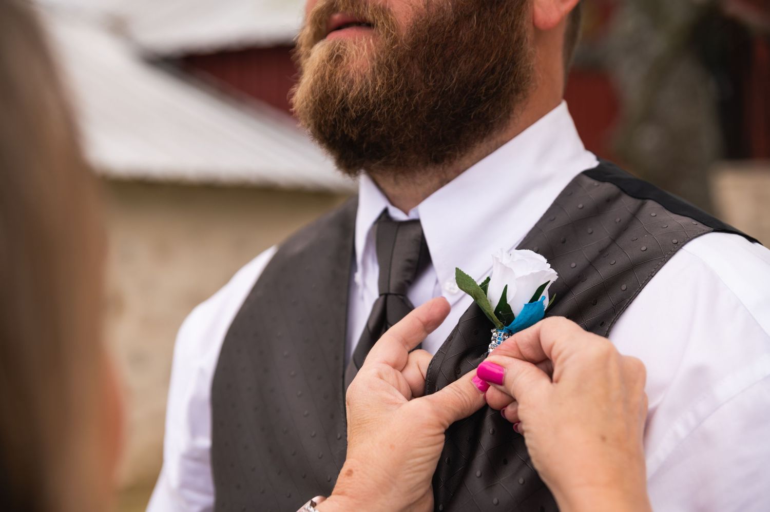 Hands pinning blue and white boutonniere on grey vest.