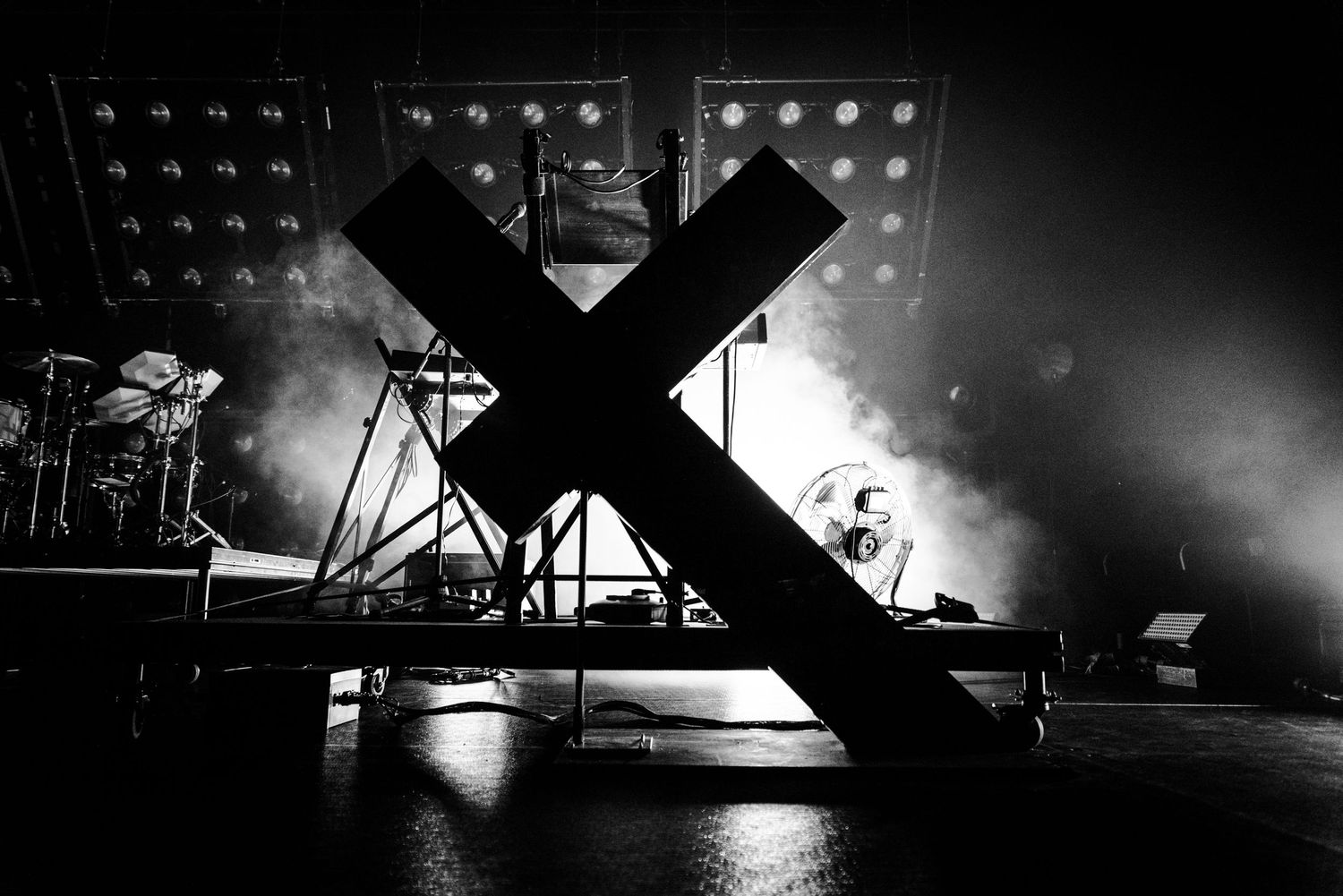 Silhouetted stage setup with large X prop and dramatic smoke effects.