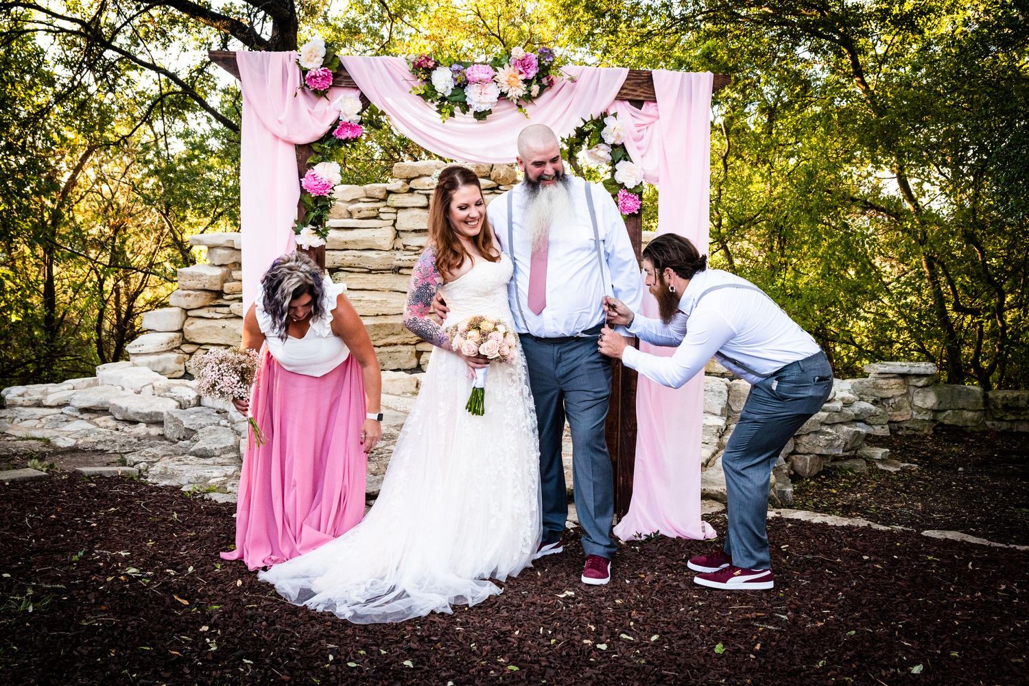 Fun candid moment of wedding party laughing under pink floral arch.