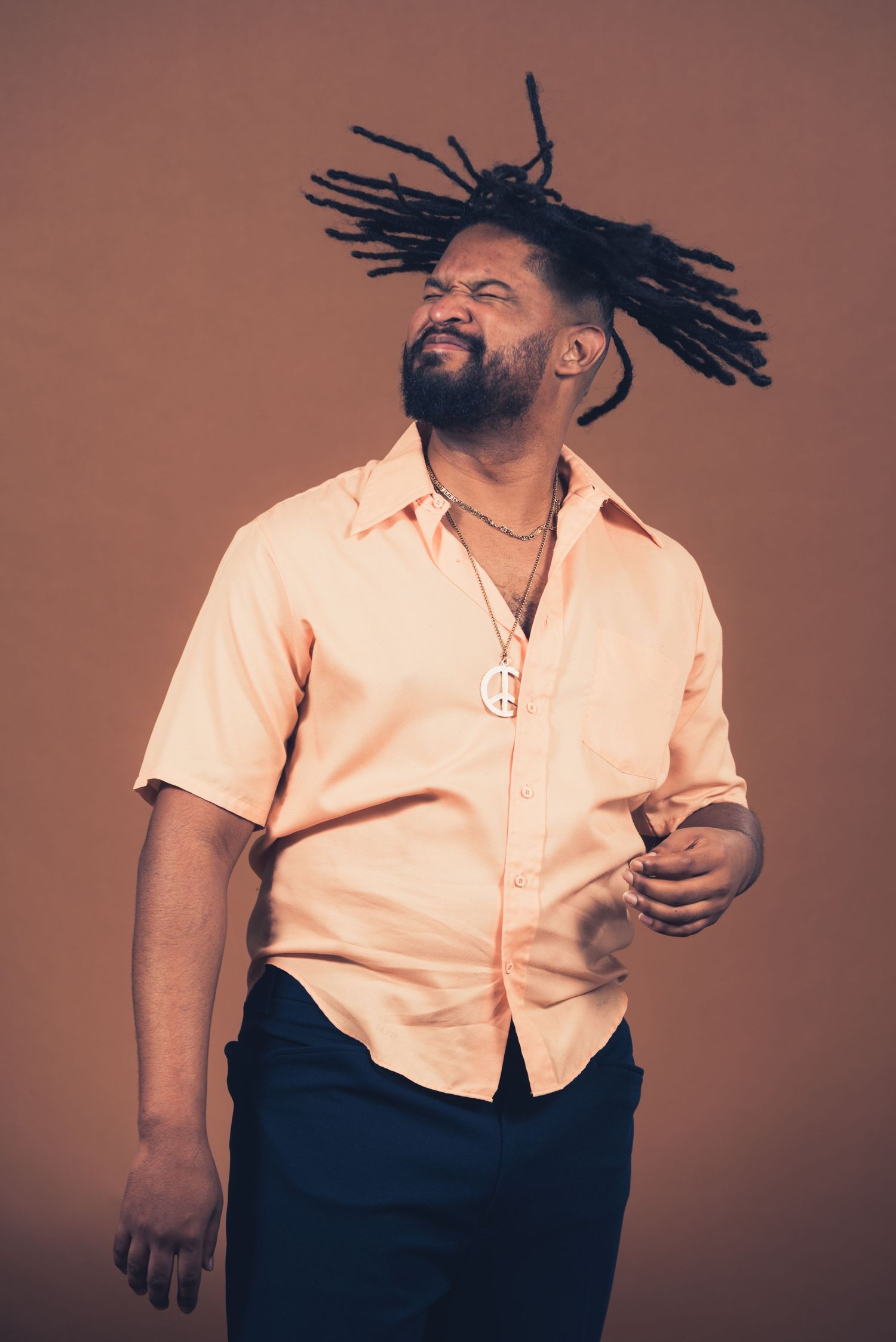 Person with dreadlocks wearing peach shirt laughs joyfully against studio backdrop.