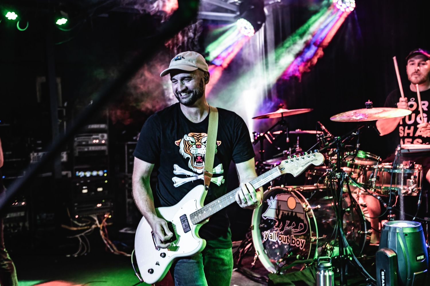 Guitarist performs on stage with colorful purple and green lighting effects at a live concert.