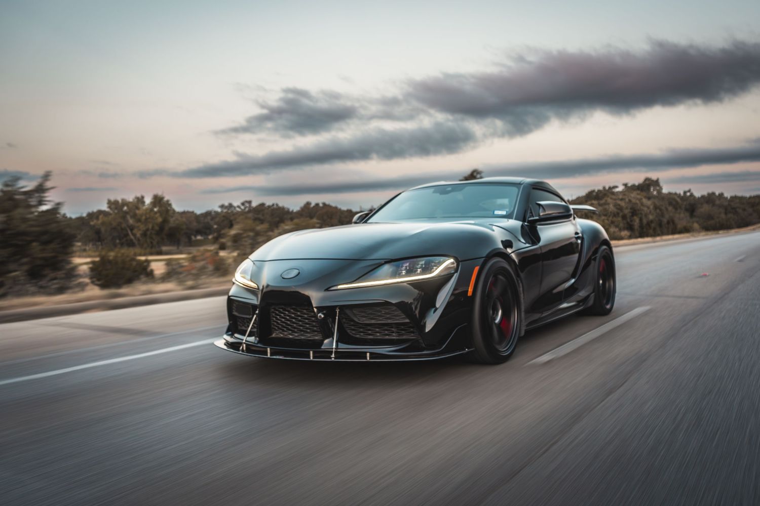 Black modified Toyota Supra with custom aerodynamics shot in motion at sunset.