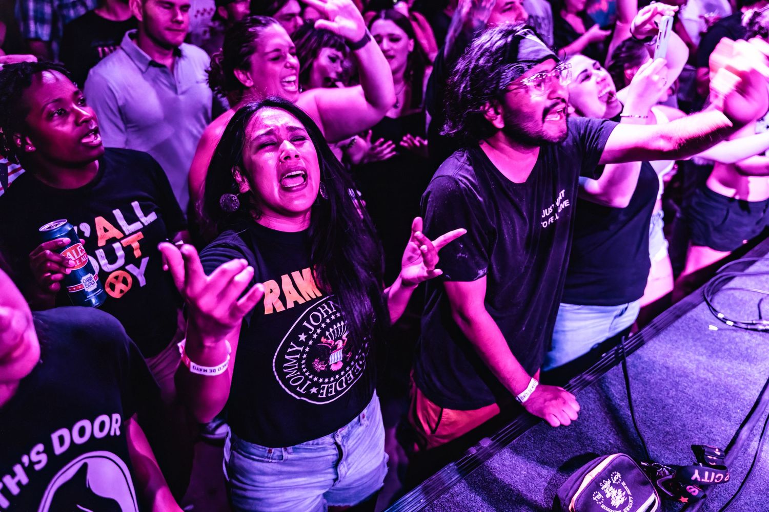 Concert audience in purple lighting cheering and raising their hands at a rock show.