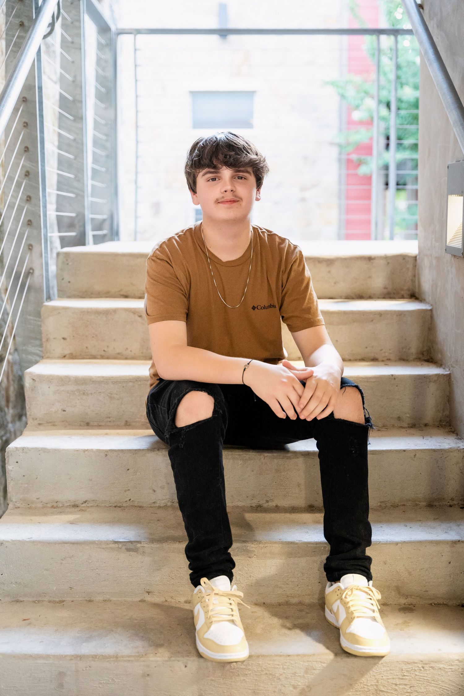 Someone in casual attire sits on concrete stairs with white sneakers.