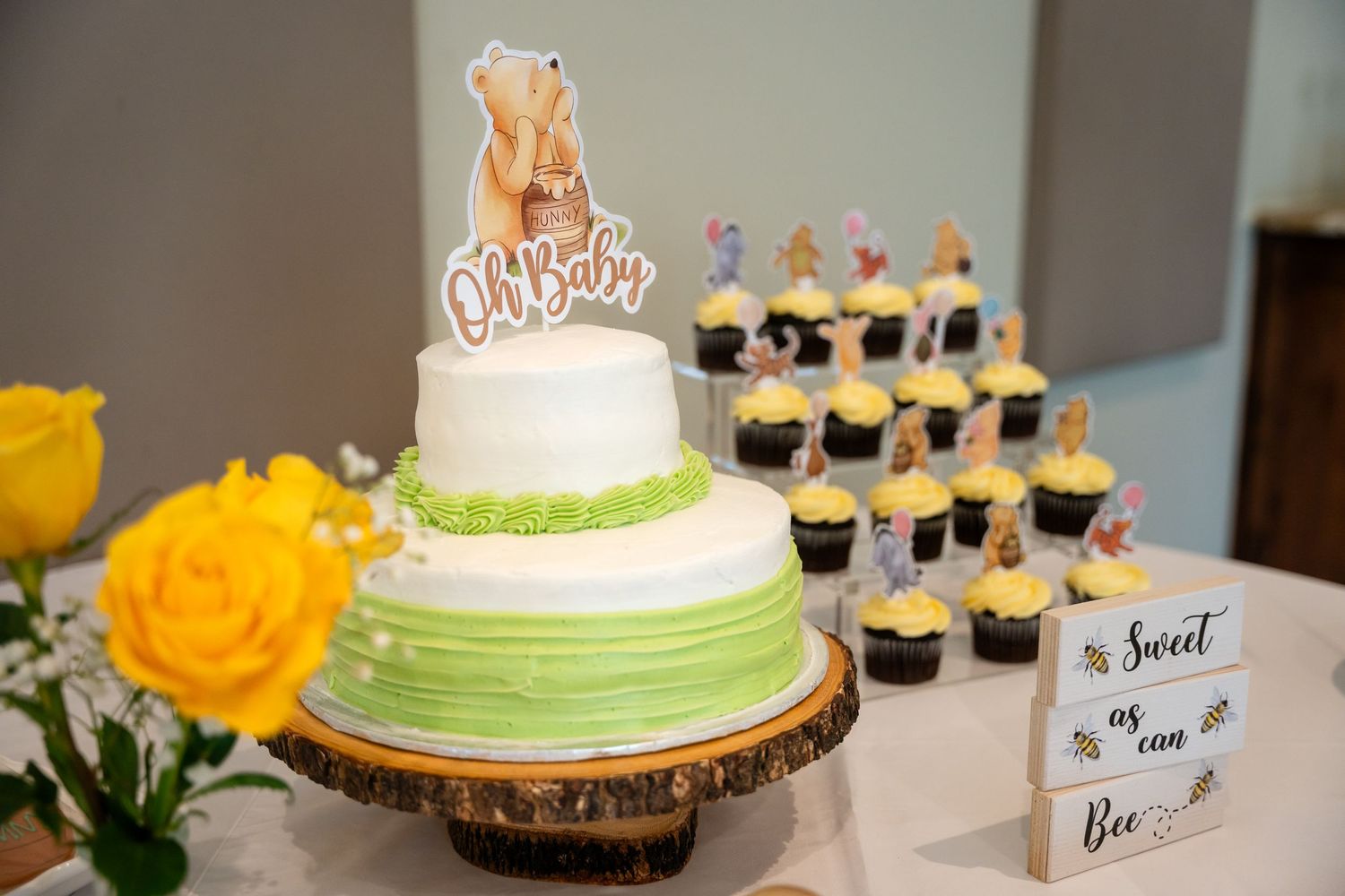Elegant two-tiered green ombre cake with honey-themed topper displayed with matching cupcakes.