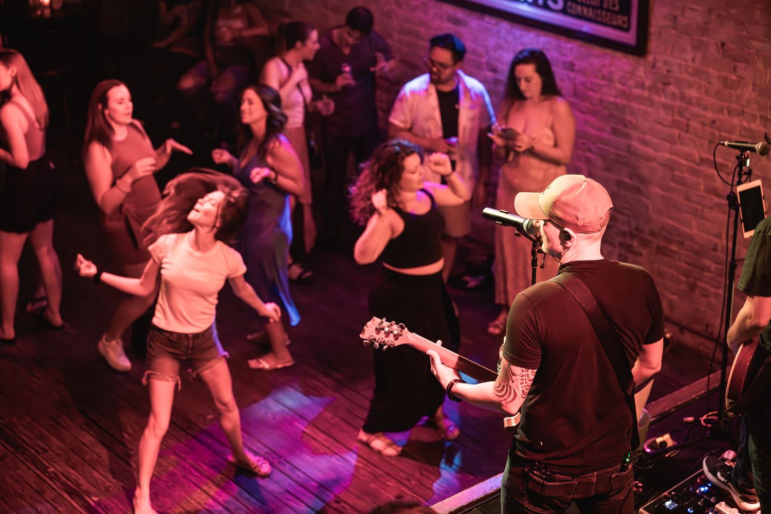 People dancing and enjoying live music at a venue with purple stage lighting.