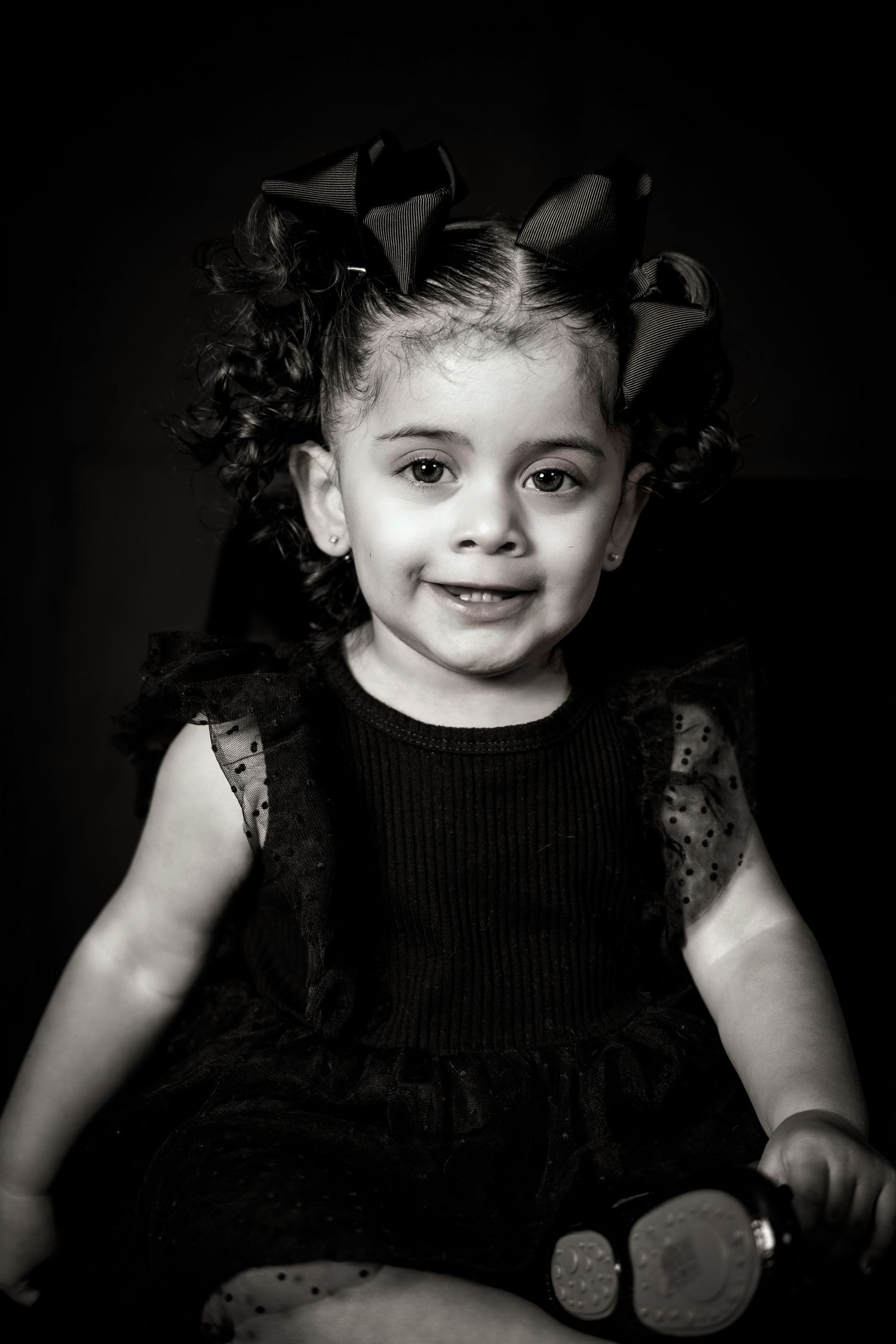 Black and white studio portrait of joyful toddler with curly hair and bows.