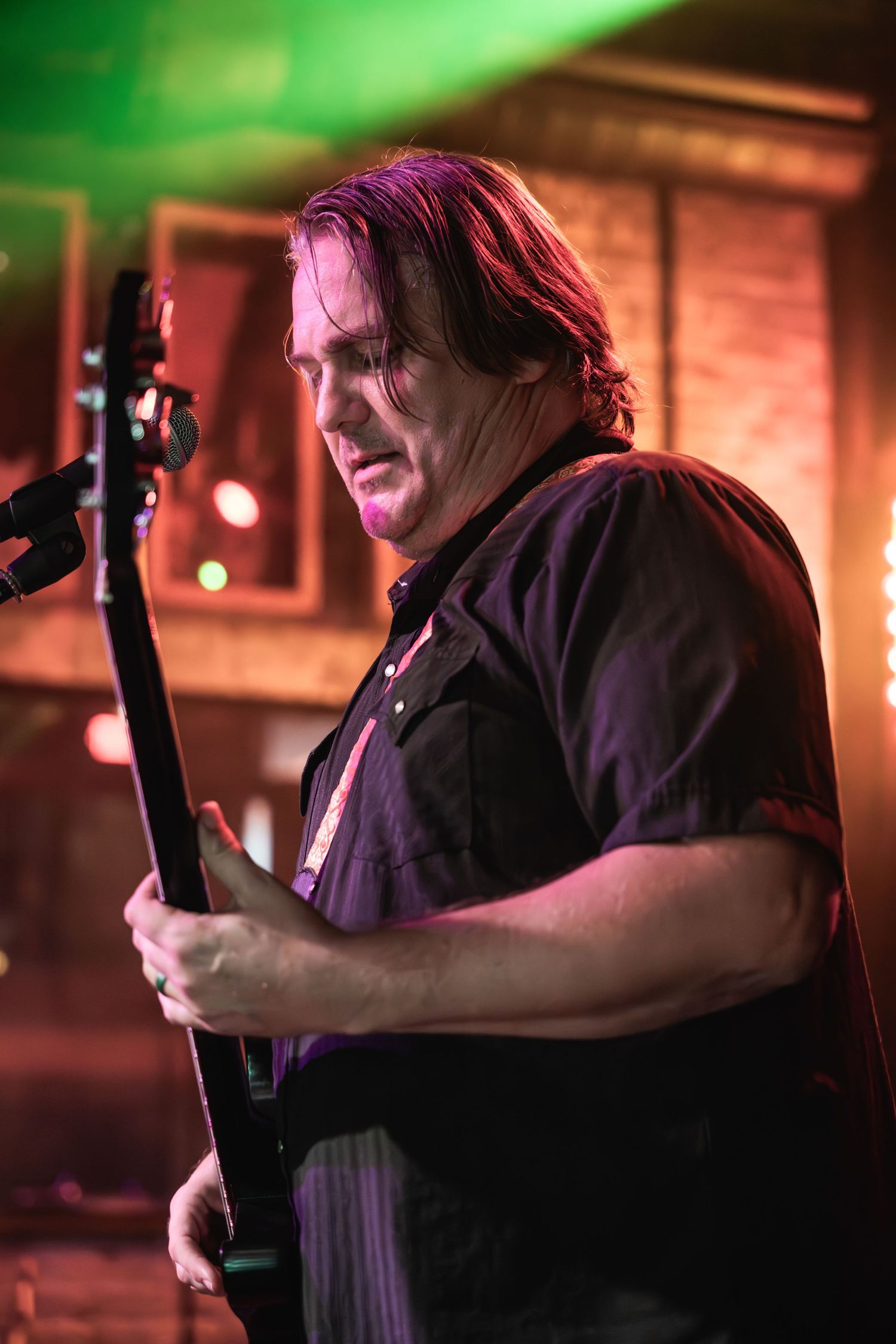 Bass player performing under dramatic red and green stage lighting at a live music venue.