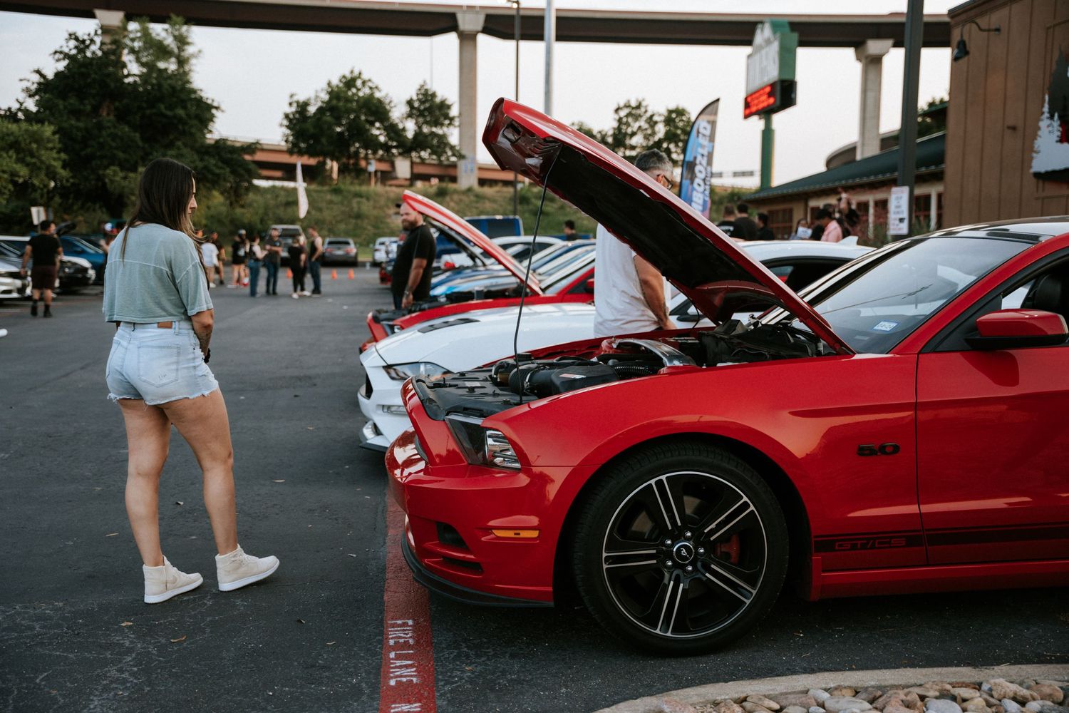 Red Ford Mustang with open hood displayed at car meet with spectators viewing.