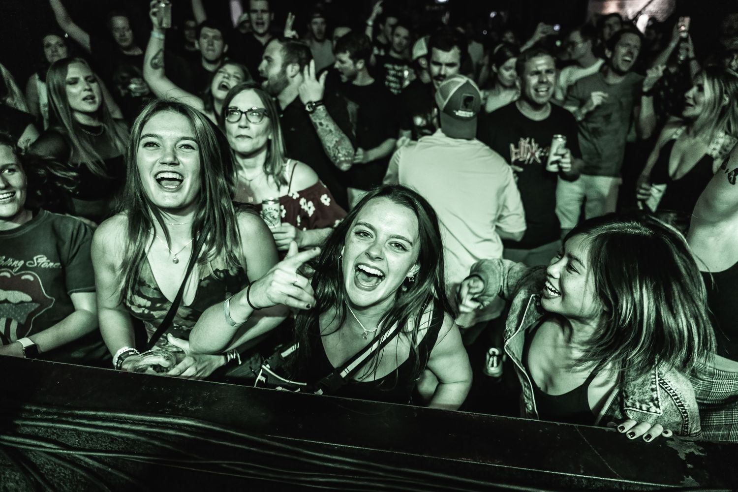 Enthusiastic crowd cheering and singing along at the front row barrier of a concert.