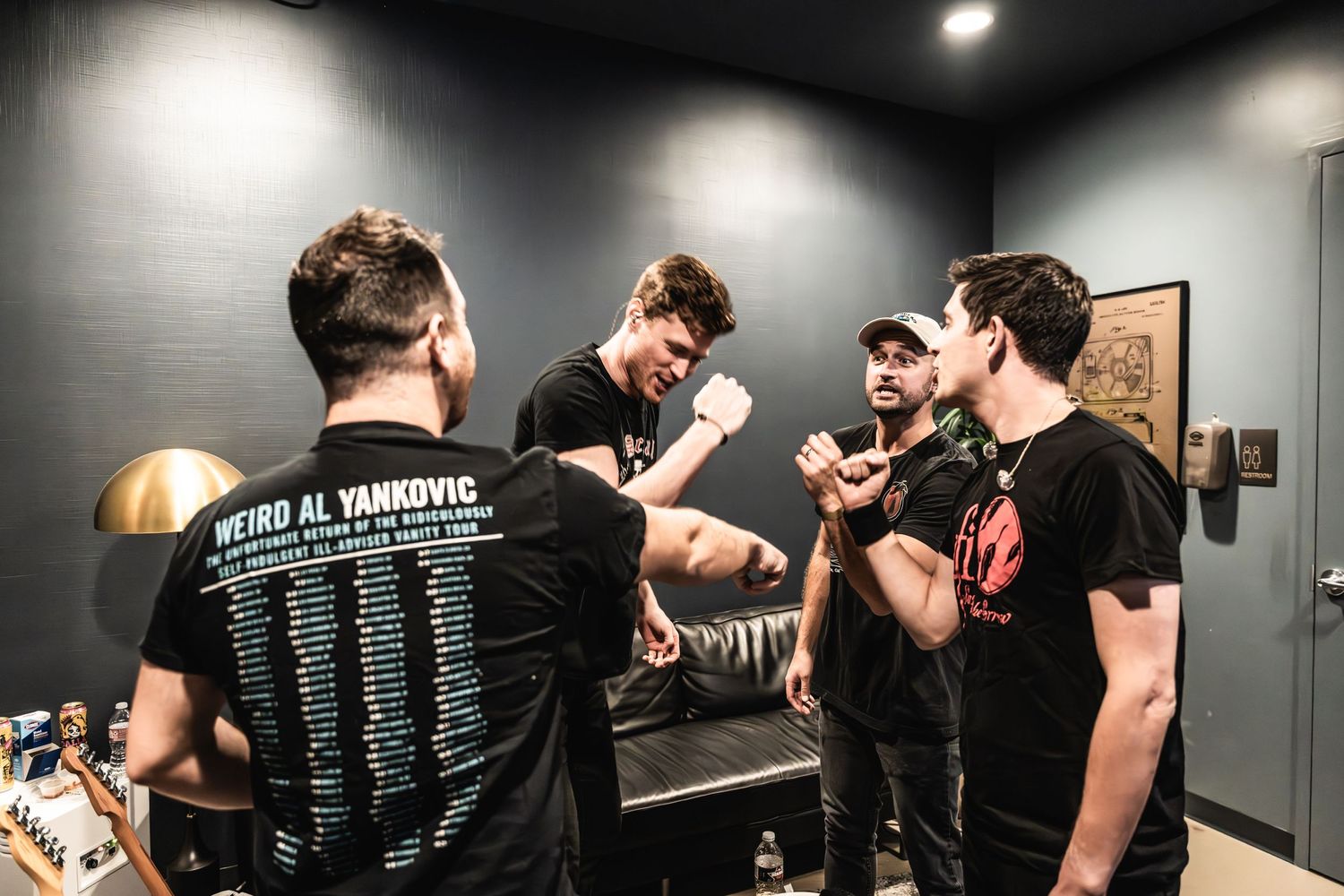 Group gathered in backstage area wearing black t-shirts and engaging in conversation.