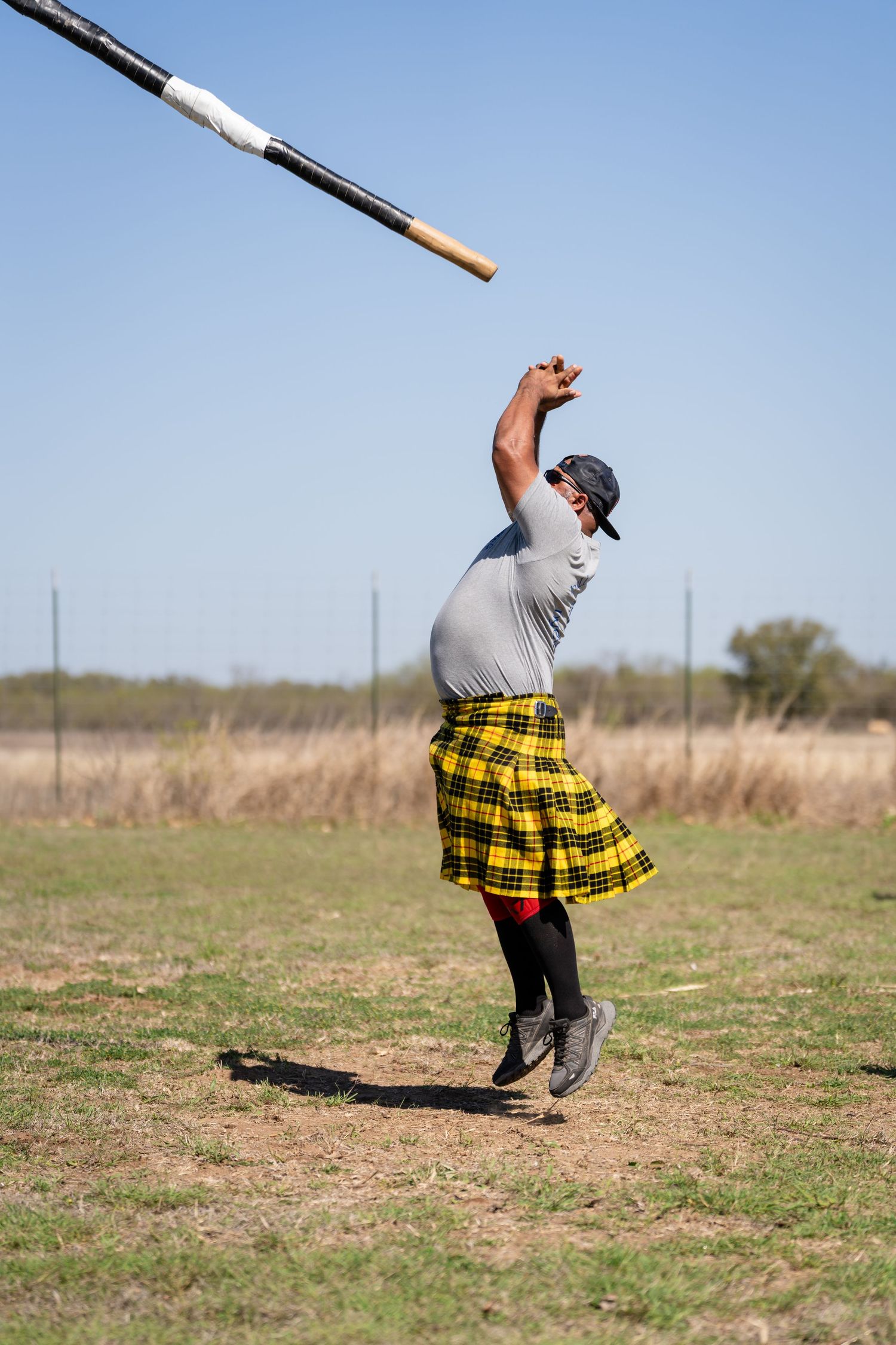Man in yellow tartan kilt tossing a caber at a Highland Games competition outdoors.