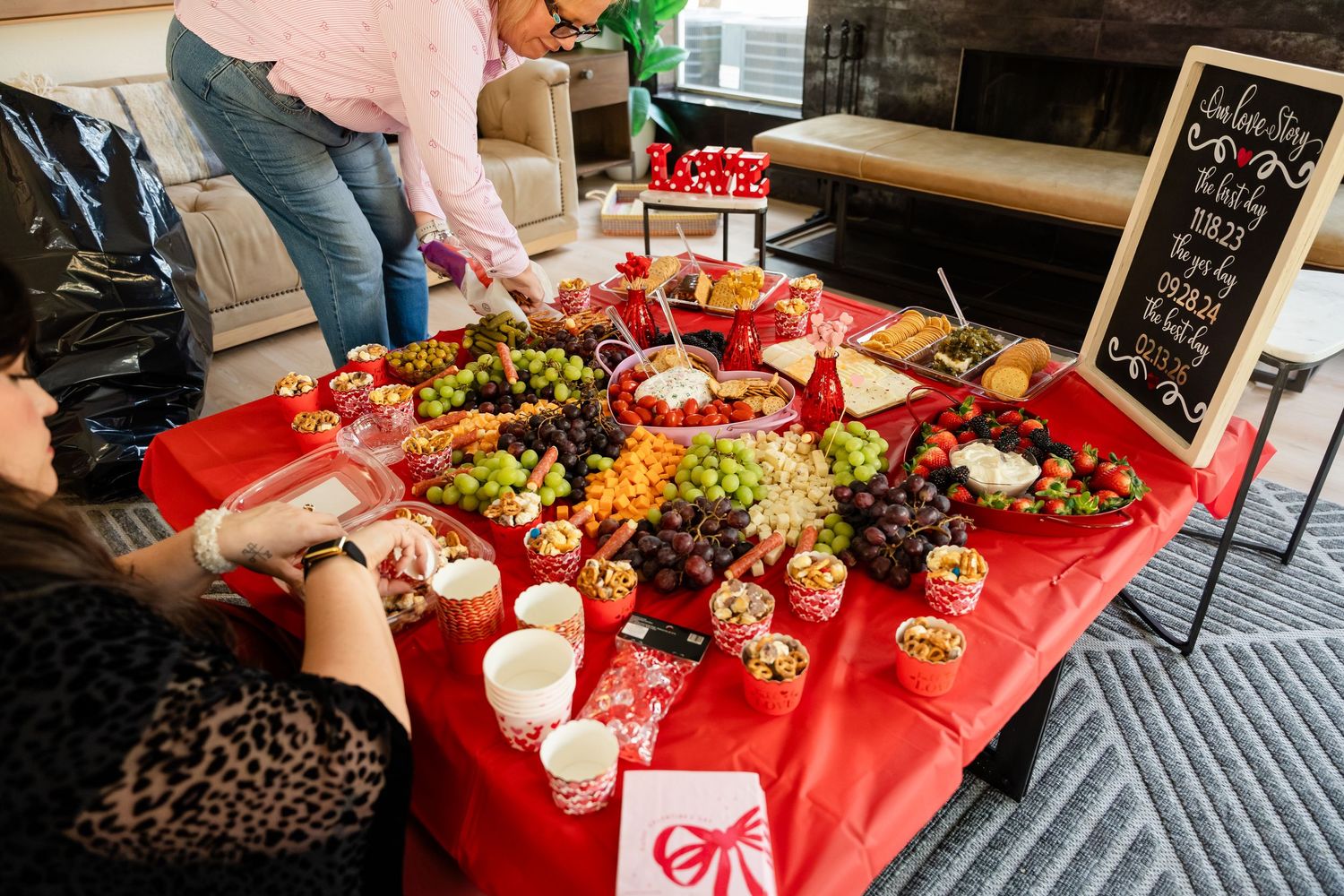 Festive red tablecloth party spread with grapes, fruits, and snacks displayed on a table with a chalkboard sign.