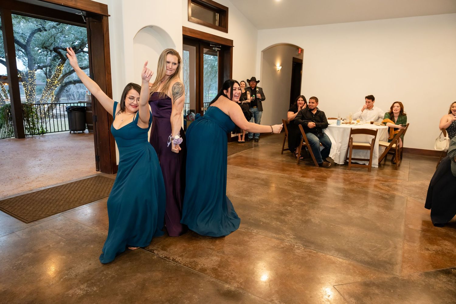 Bridesmaids in teal gowns dancing joyfully at a wedding reception in an elegant venue.