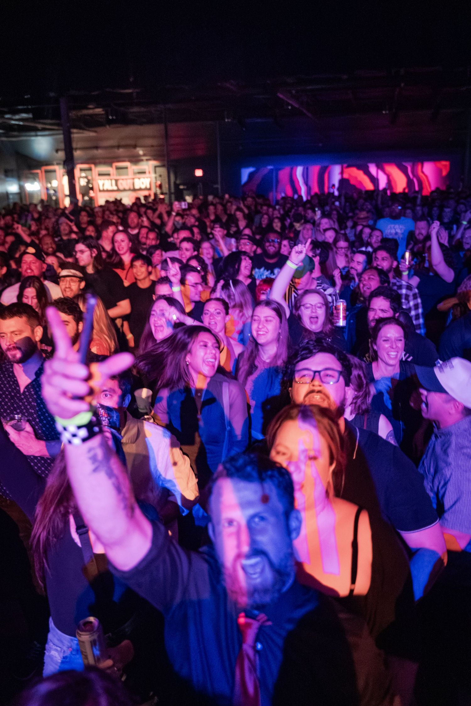 Energetic concert crowd enjoying a live music event under colorful blue and purple stage lights at an indoor venue.