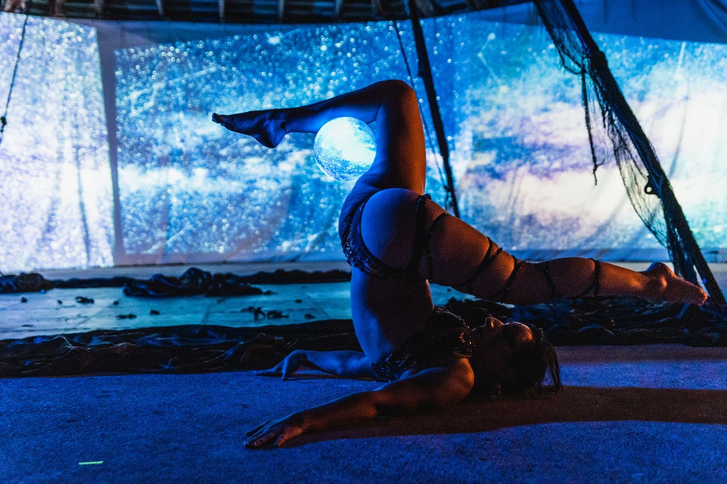A silhouetted figure performs a yoga pose on a mat against a dreamy blue-lit backdrop with fabric draping.