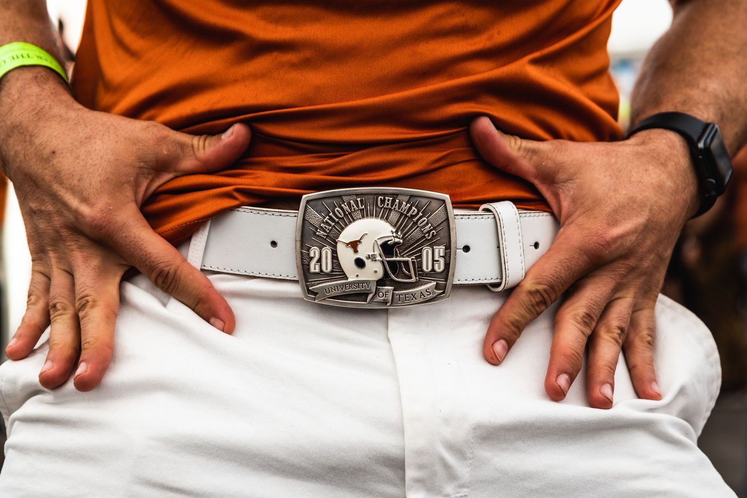 Close-up view of hands wearing a brown leather belt with ornate silver buckle against white clothing.