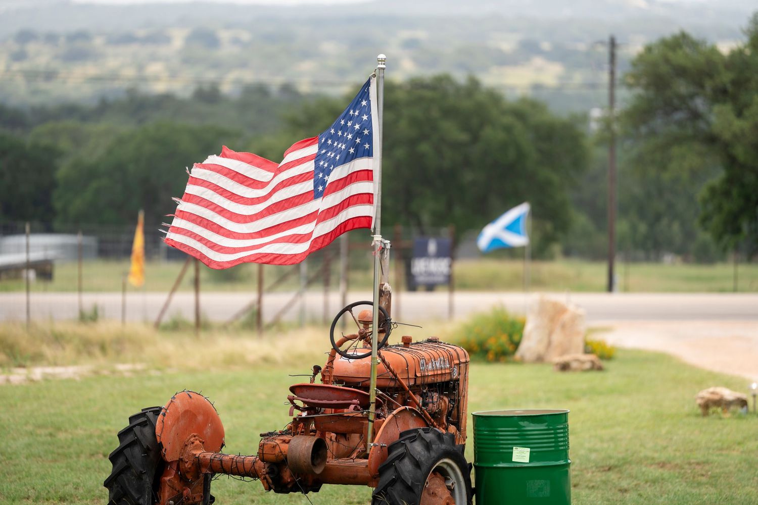 American flags wave in the wind behind a vintage red tractor parked in a rural field.