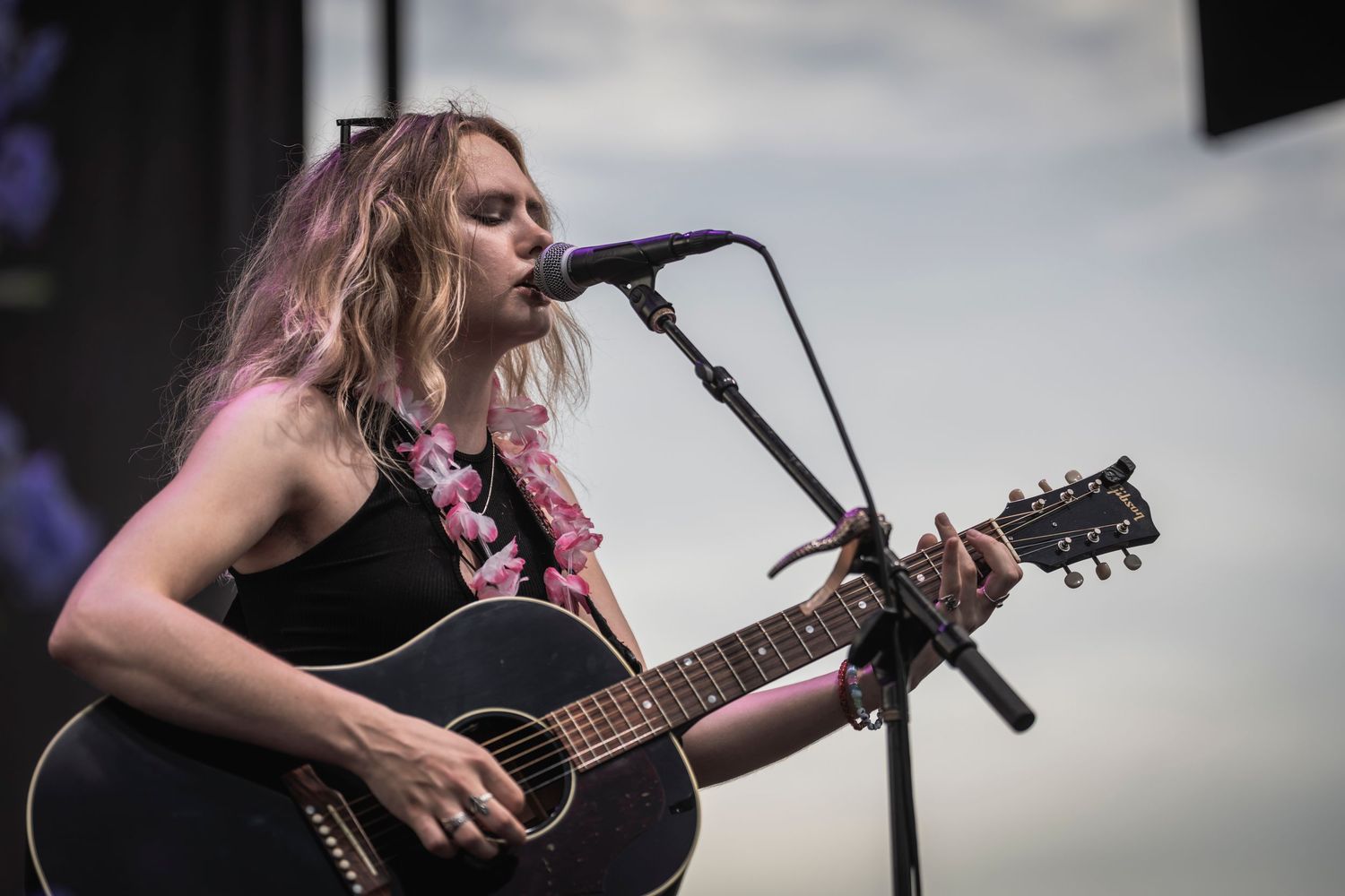A performer plays acoustic guitar and sings into a microphone on stage during a live musical performance.