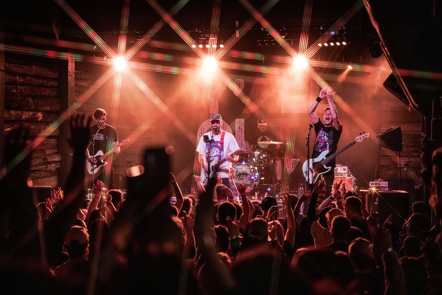 Concert performers on stage bathed in dramatic orange lighting while entertaining an energetic crowd at a live music venue.