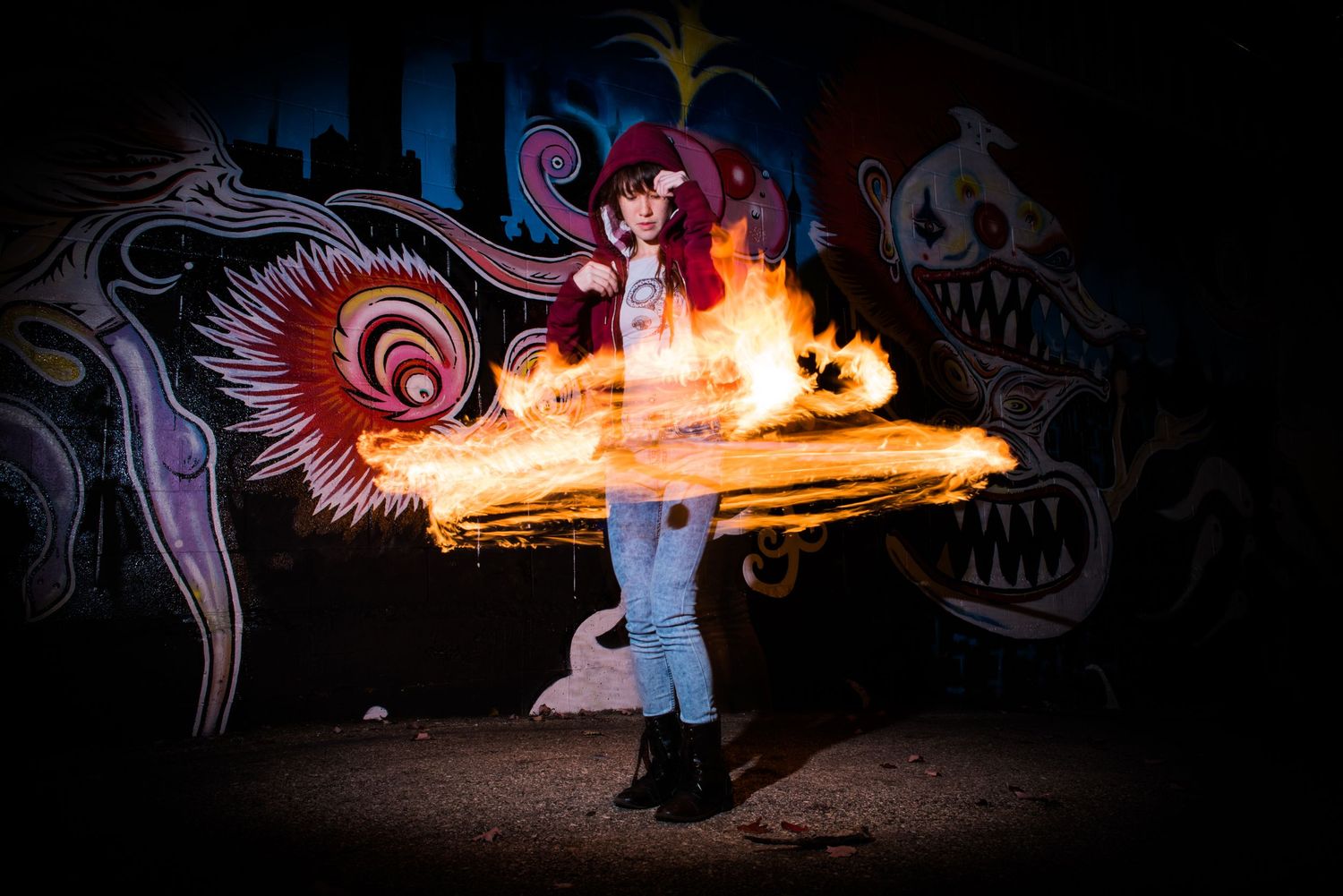 Fire performer creates mesmerizing light trails against dark background with colorful dragon art mural.