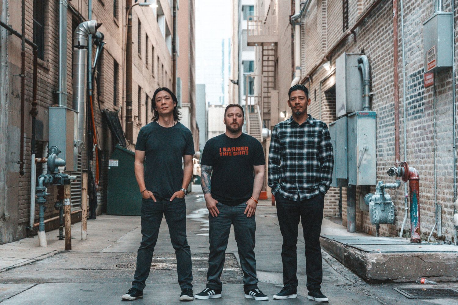 A group stands together in a casual pose against an urban brick alley backdrop in coordinated casual outfits.