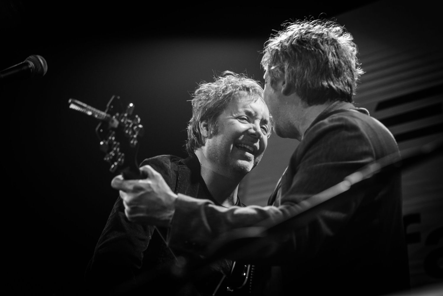 Black and white photo of two performers sharing an energetic moment on stage with guitars during a concert performance.
