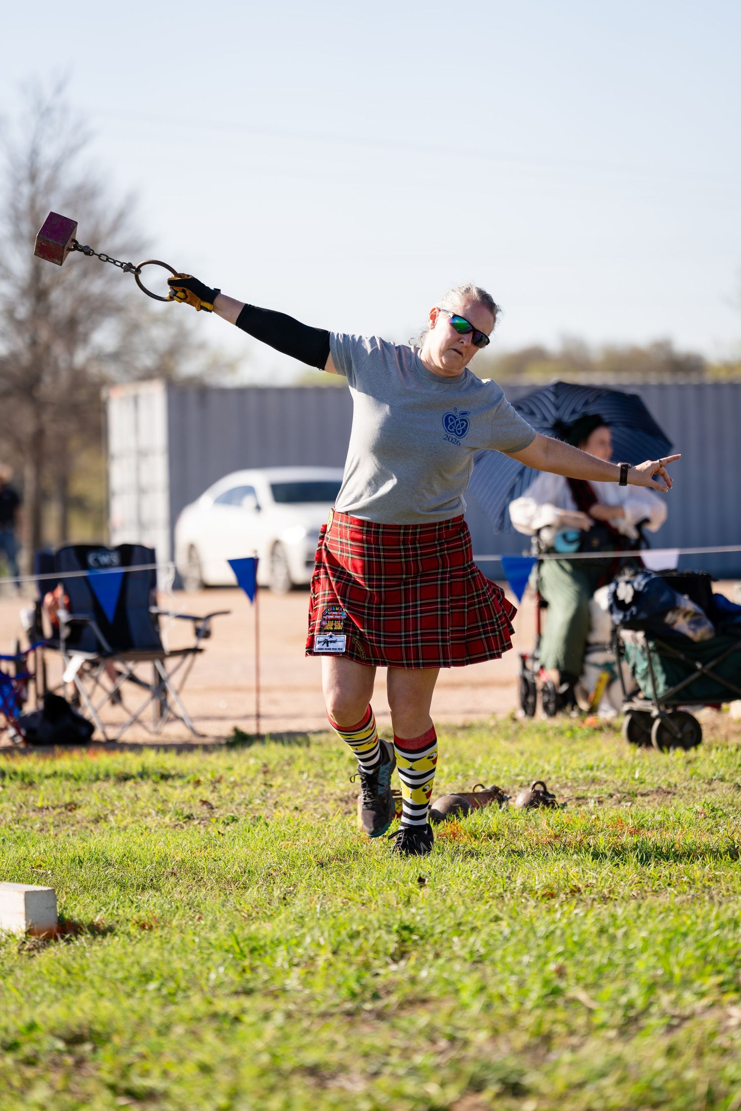 Athlete in red tartan kilt competes in Highland Games weight throw event on grass field.