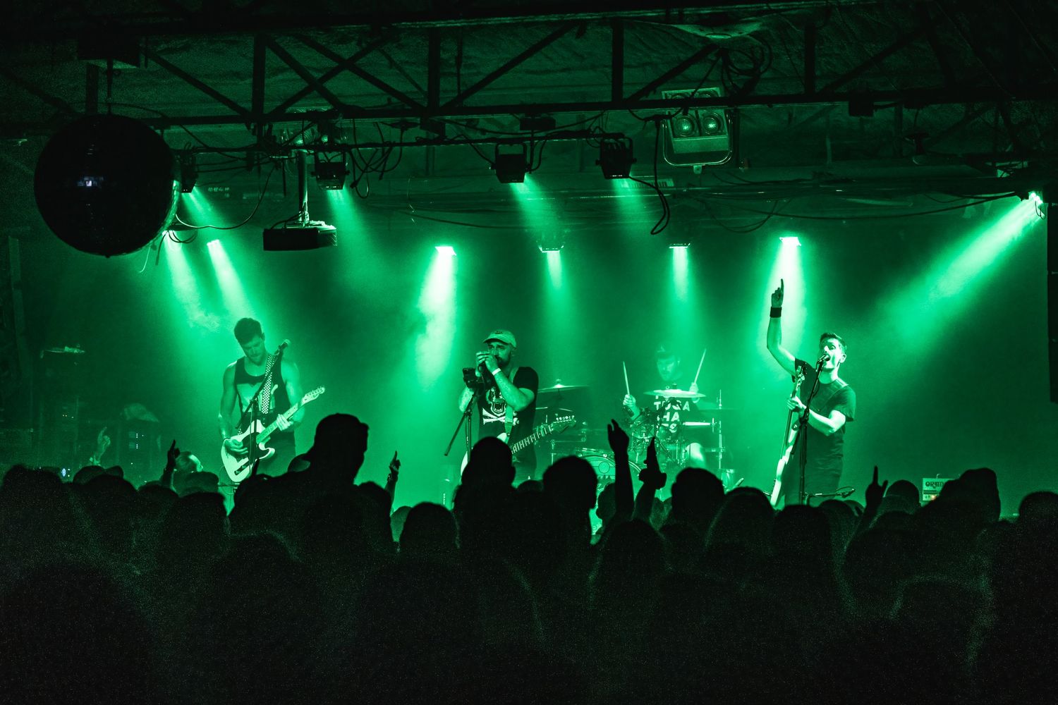 Band silhouettes perform on stage bathed in bright green lighting effects above a crowd.