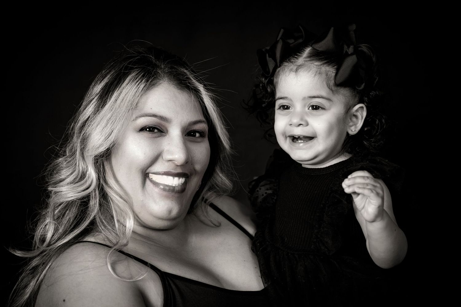 Black and white studio portrait of a parent and child sharing a joyful moment against dark background.