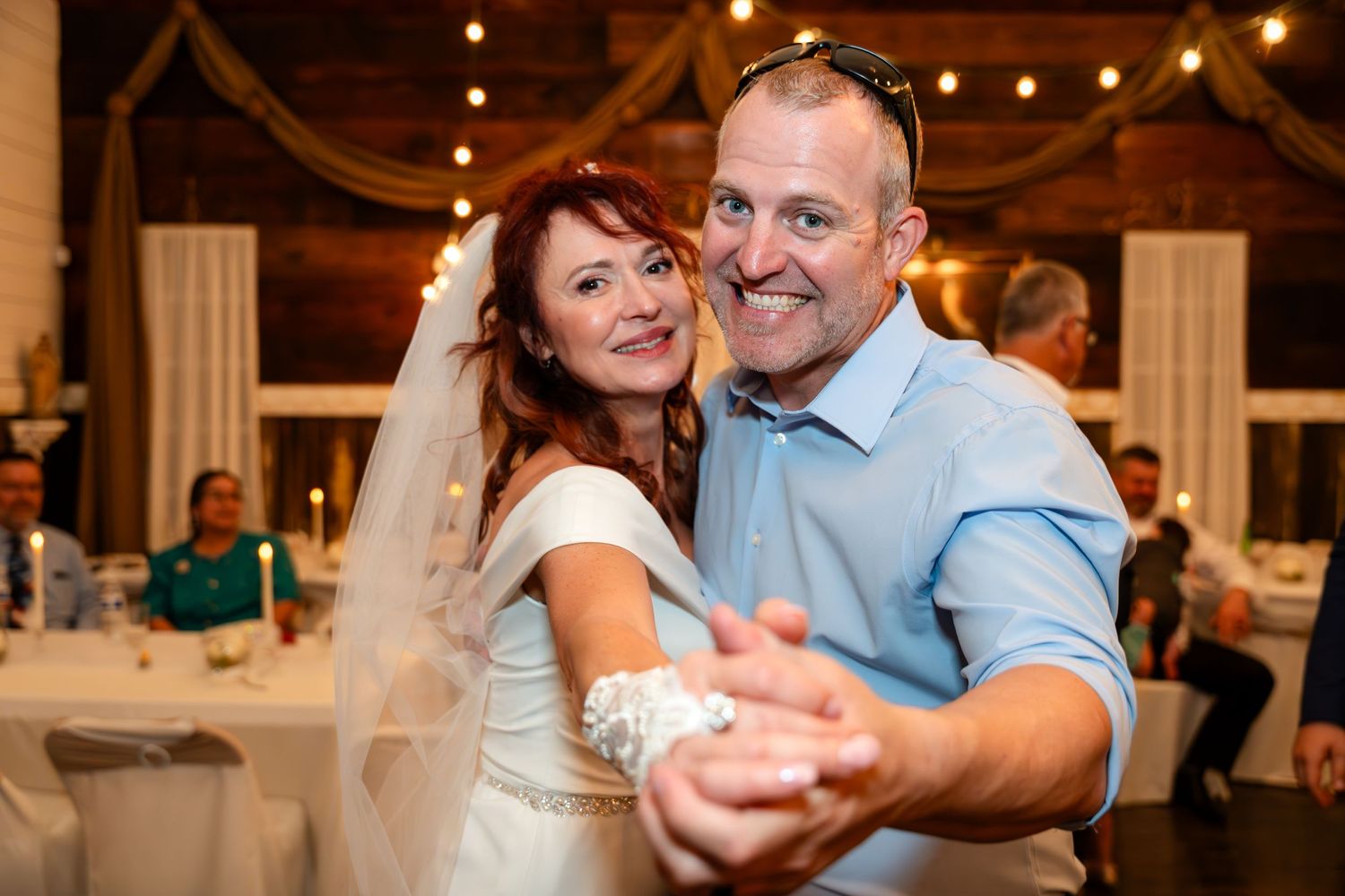 Couple dancing together at their wedding reception in a rustic venue with string lights.
